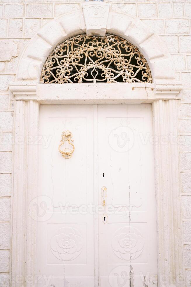 White wooden door on the stone facade of an ancient building with a forged arch photo
