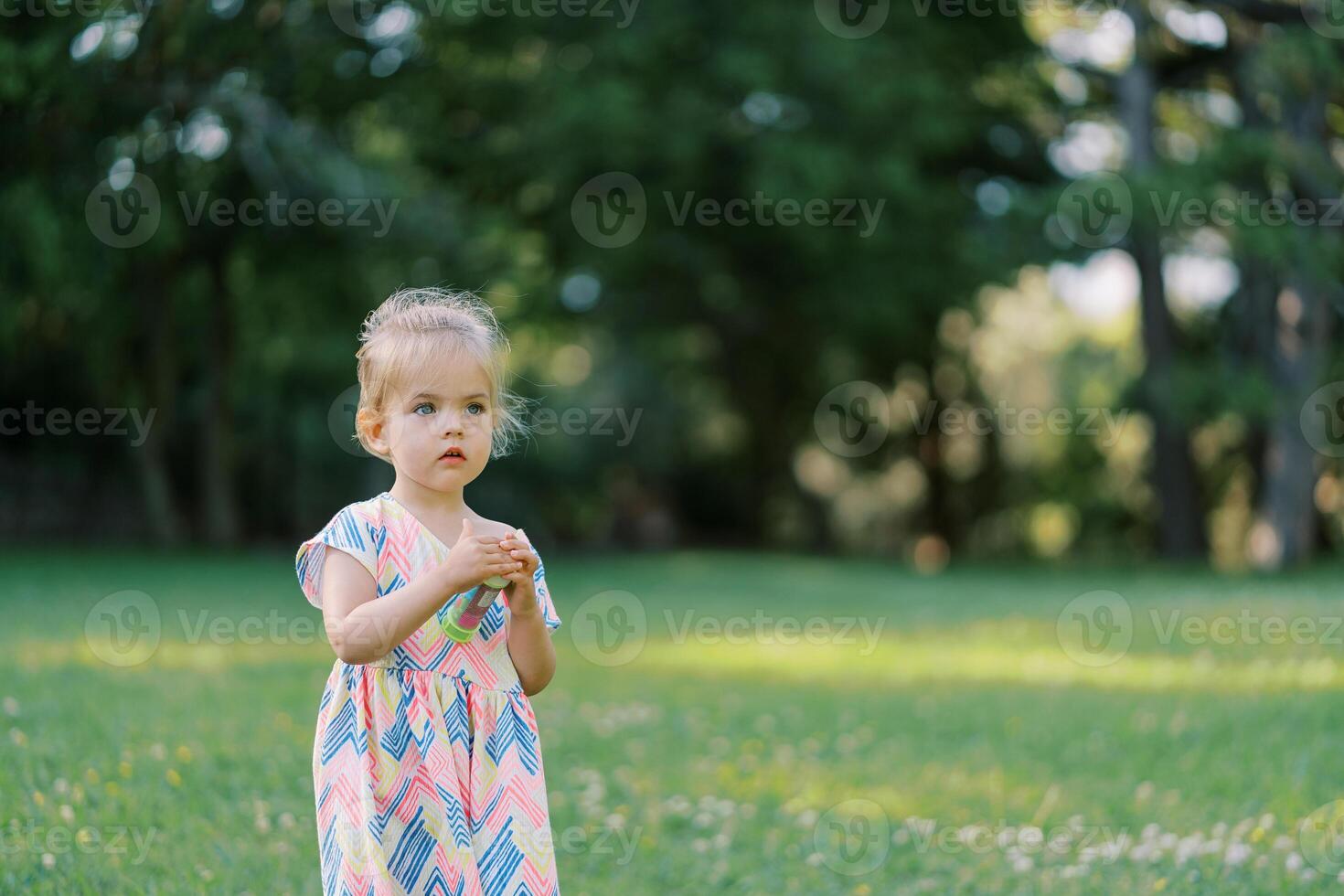 Little girl is standing on a green meadow with a bottle of soap bubbles in her hands photo