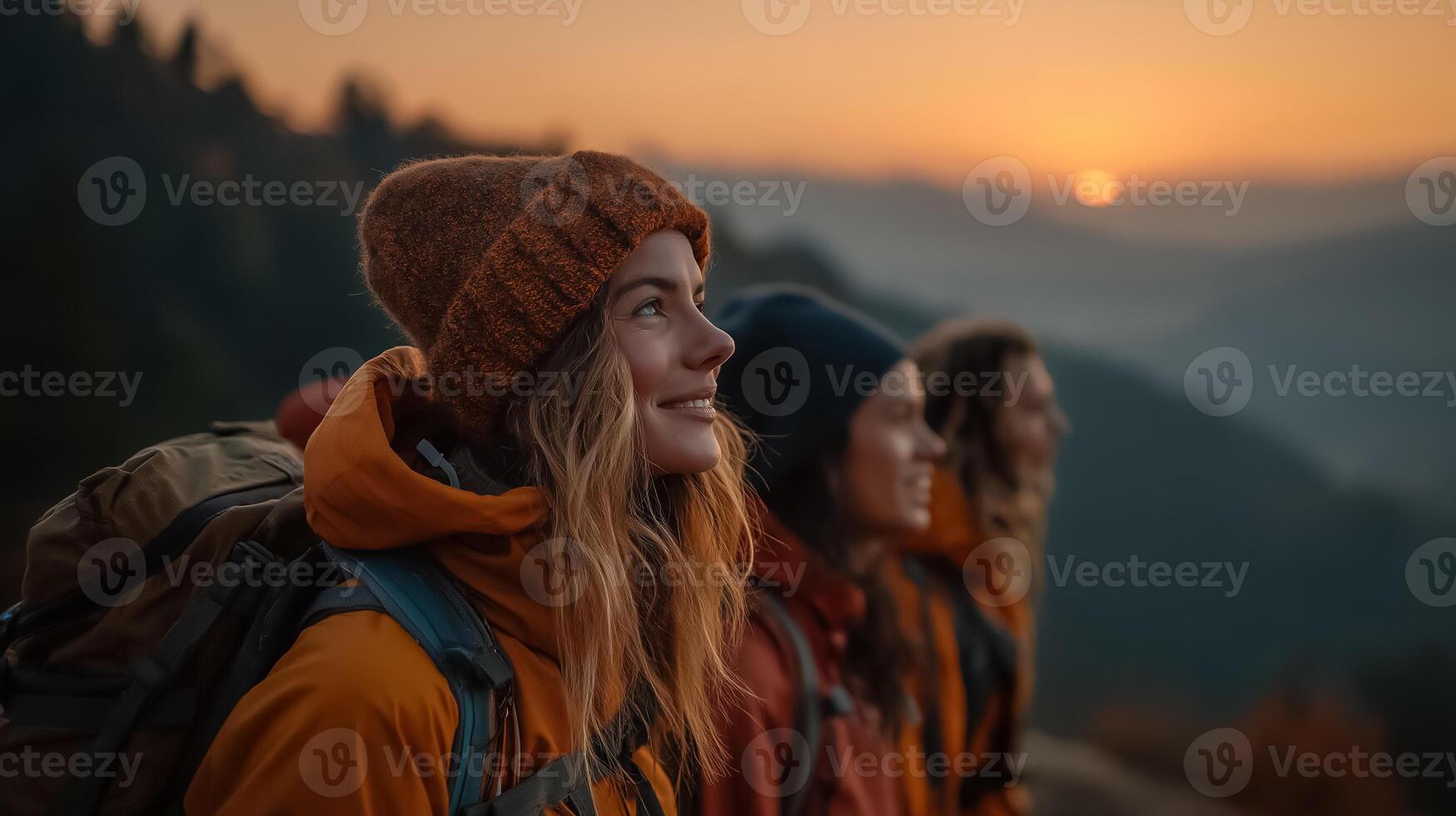 Three women with backpacks standing on a mountain at sunset photo