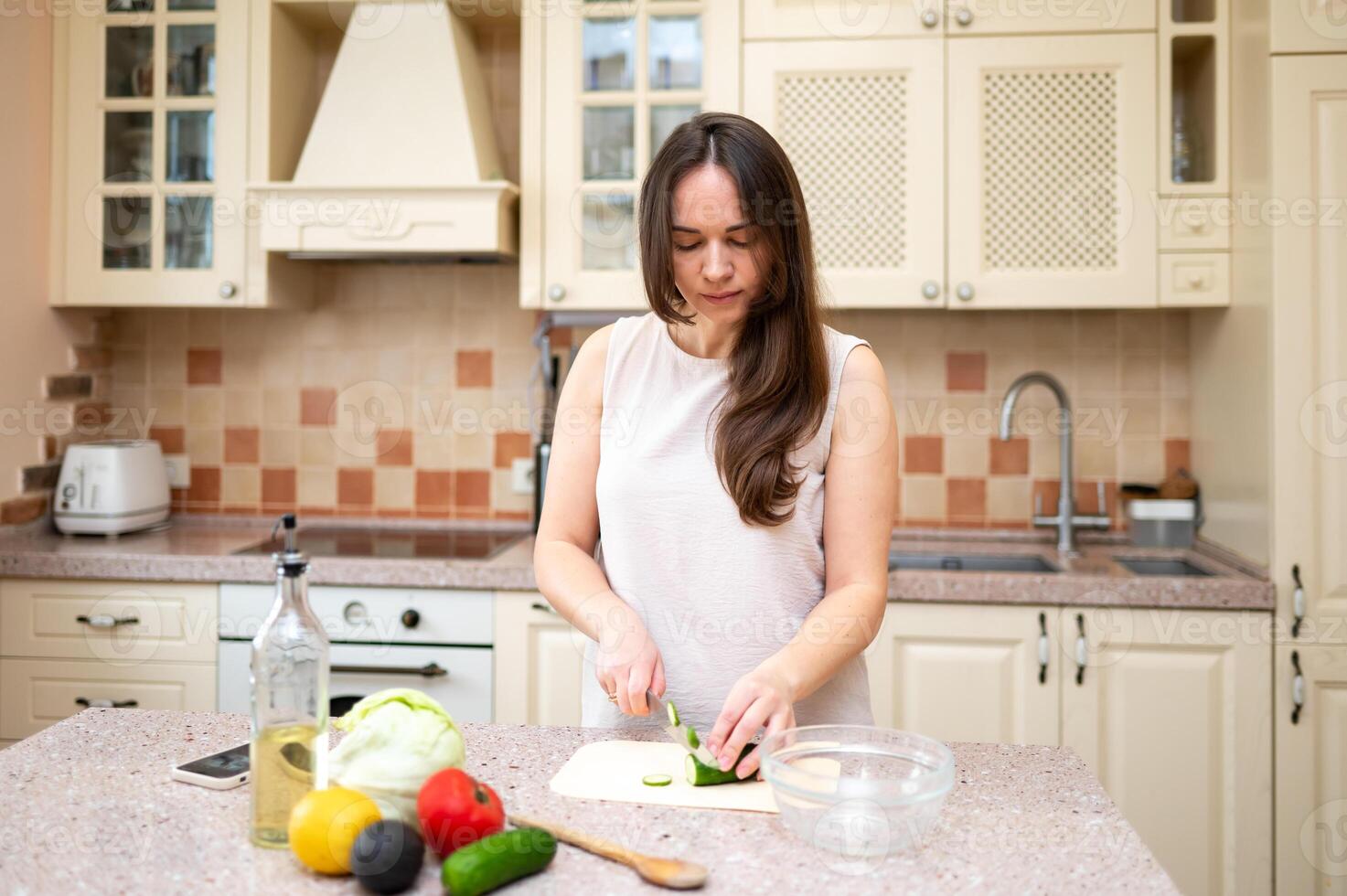 woman using smartphone while preparing fresh vegetable salad in cozy kitchen. Healthy lifestyle, home cooking and online recipe inspiration photo