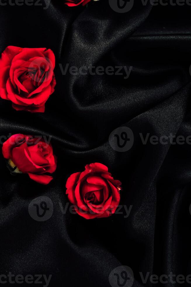 Deep red roses lay gracefully upon a smooth black fabric, highlighting the rich colors and textures of the arrangement. photo