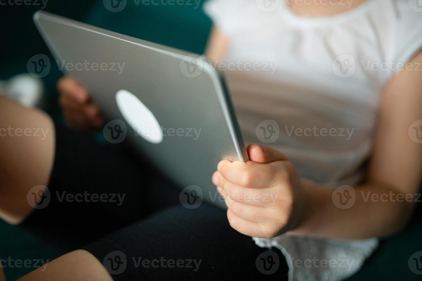 Close up of little girl holding tablet lying on sofa at home alone, happy preschool child looking at modern device screen, watching cartoons, chatting online on social network, having fun. photo