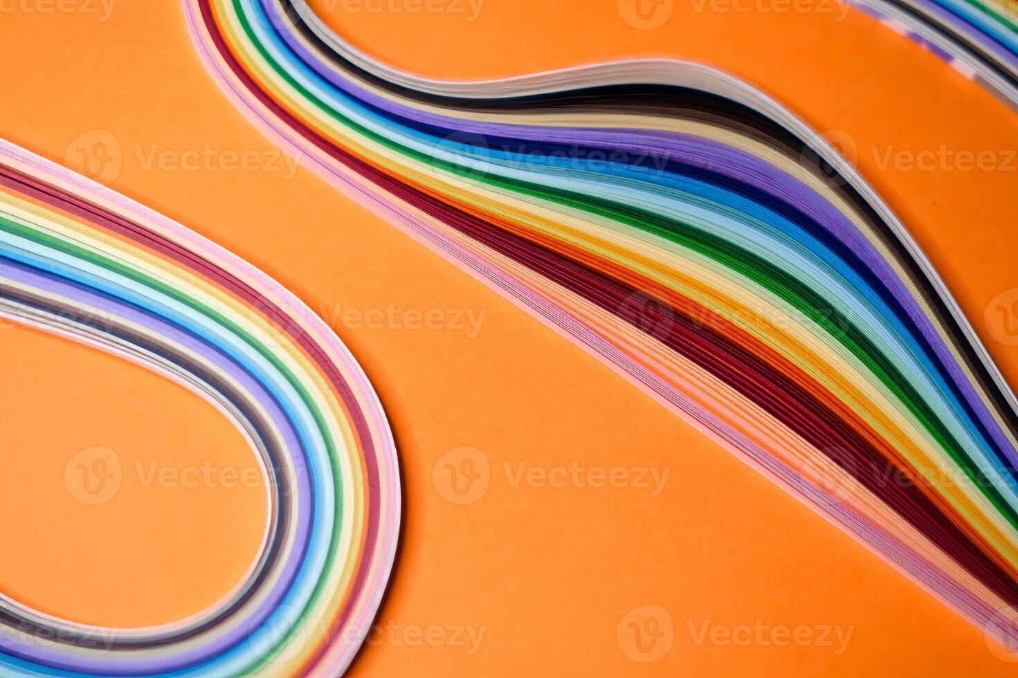 Colorful quilling paper strips arranged in smooth, flowing curves on a vibrant orange background. photo