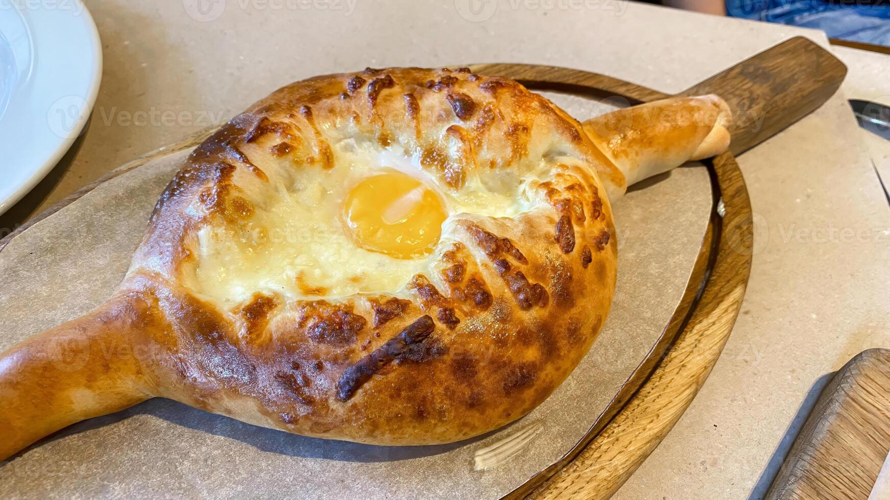 Traditional Georgian khachapuri with melted cheese and egg in the center, served hot on a wooden board photo