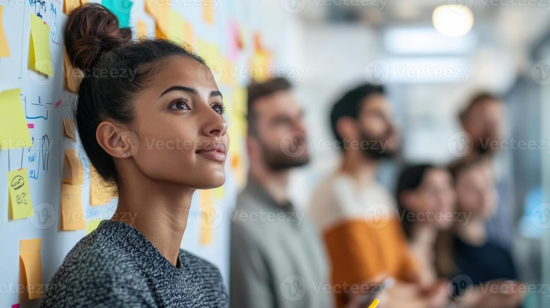 A small team of multinational delegates is engaged in a brainstorming session surrounded by sticky notes and diagrams taped to the walls. The atmosphere is dynamic with each participan photo