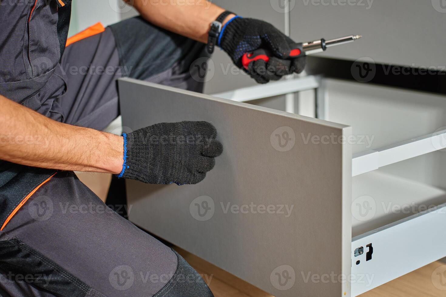 Man assembling kitchen drawer in modern cabinet using screwdriver. Handyman installing and adjusting drawer slide mechanism in contemporary kitchen. Furniture installation photo