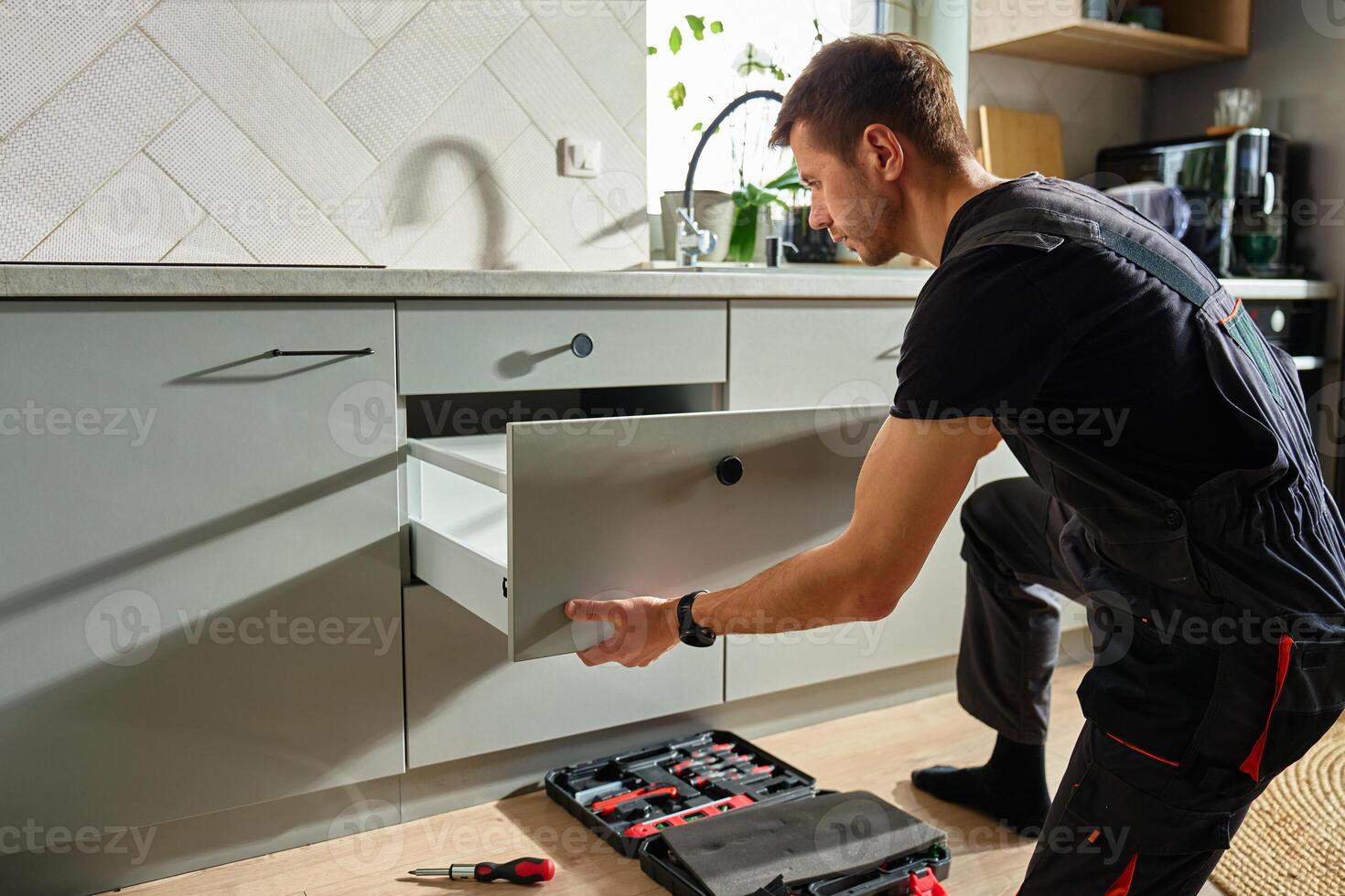 Male carpenter installing and adjusting drawer front in modern kitchen cabinet photo