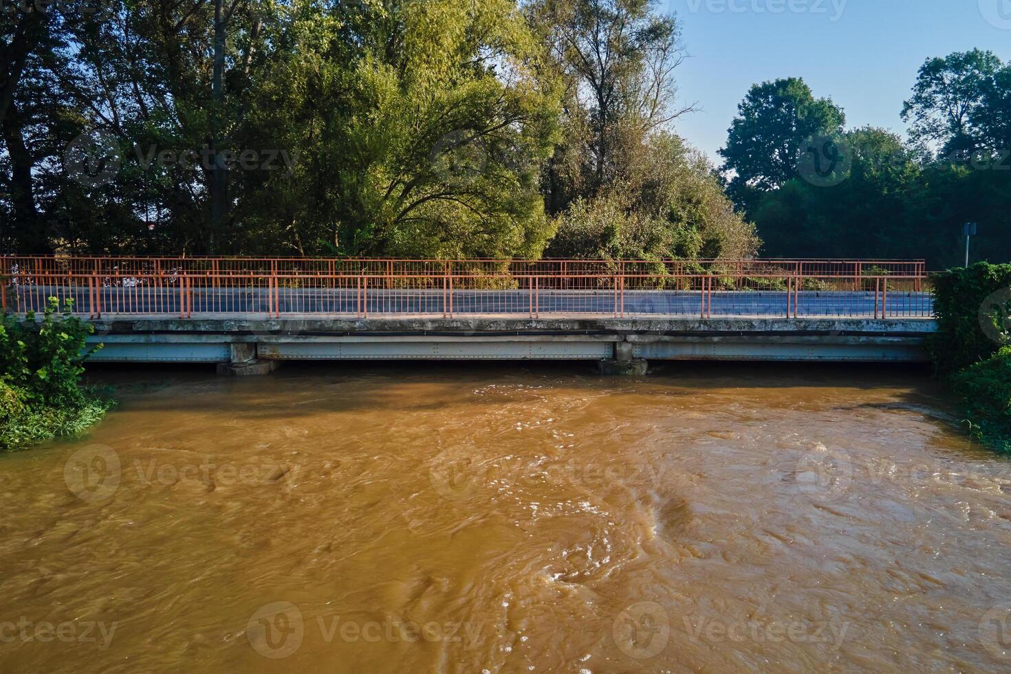 Brown muddy water flows under road bridge. Flooded river after heavy rainfall. Natural disaster photo