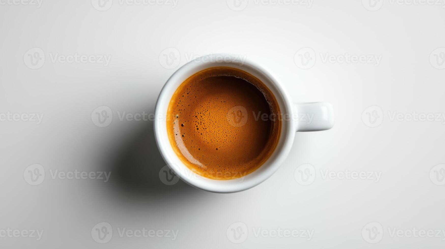 Espresso coffee in white cup sits on a plain white background. Focus is on liquid surface and creamy foam from overhead view. photo