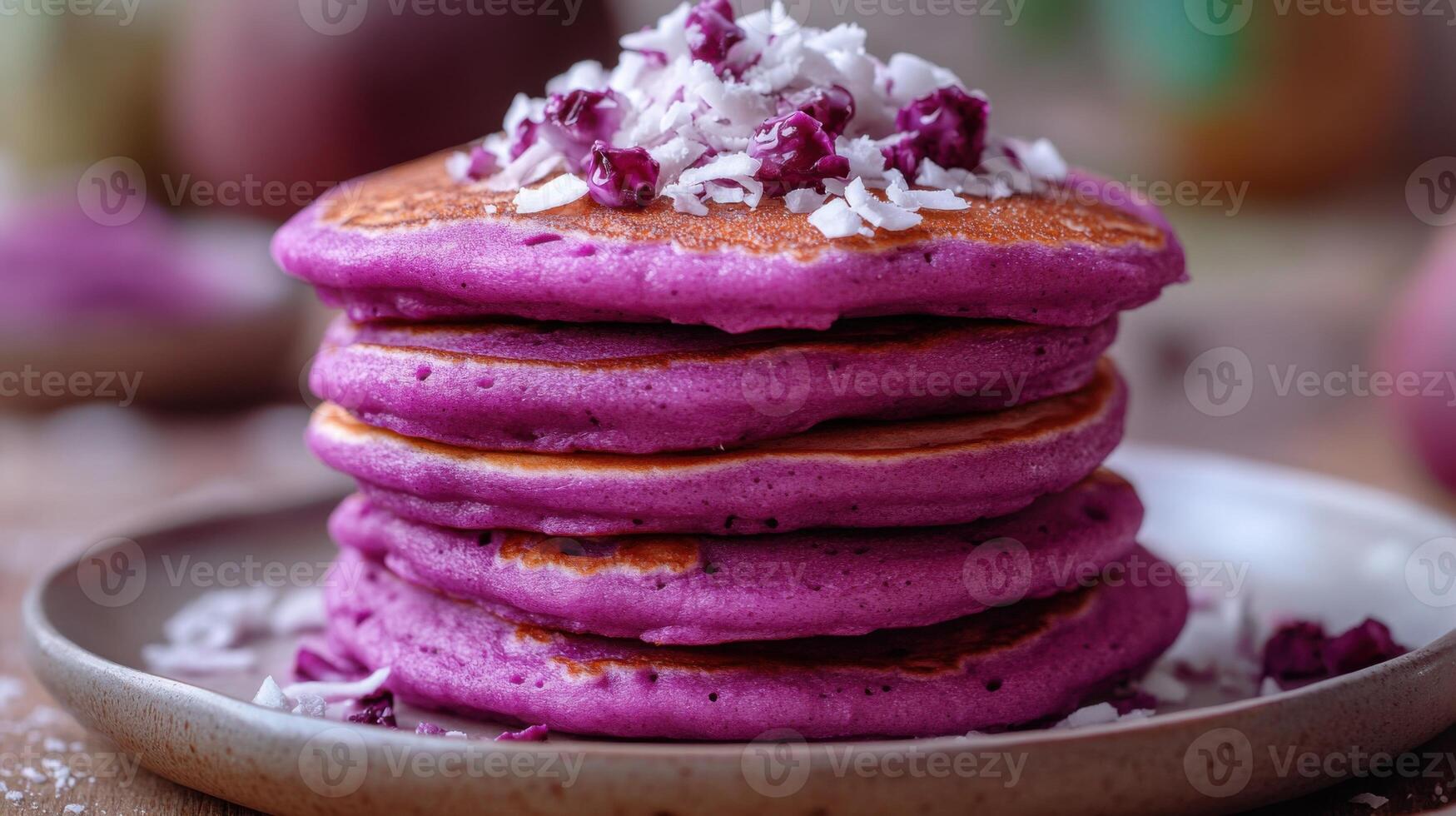 Stack of purple pancakes on plate. Breakfast food is topped with shredded coconut. The setting is a wooden table surface. photo