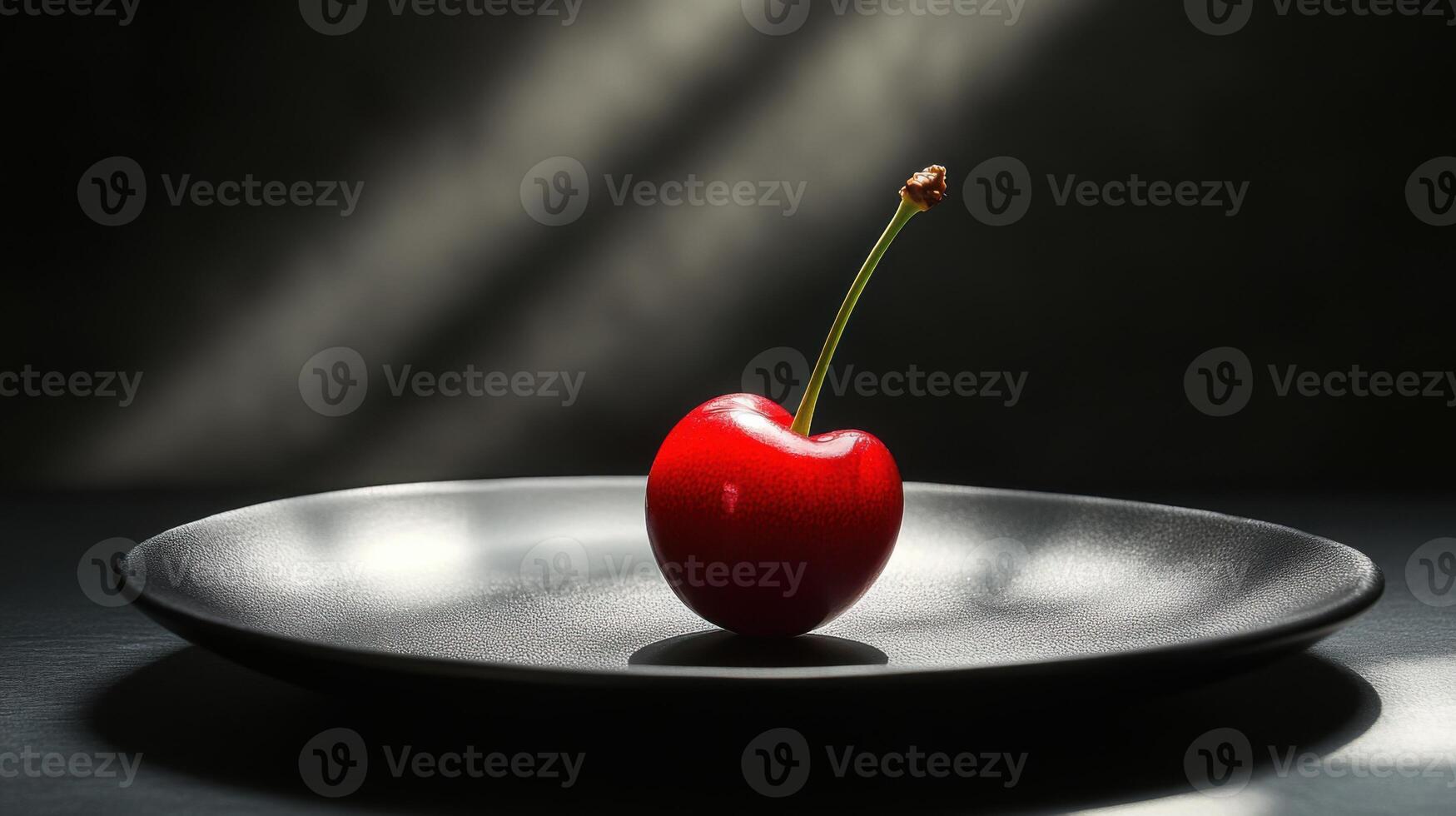 Single red cherry sits on a dark plate. Light shines on the food with a black background. Simple and minimalist still life. photo