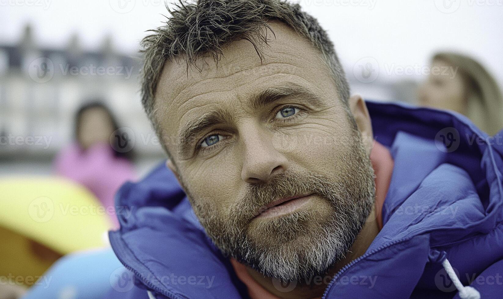 A man with a beard and blue jacket looking at the camera photo