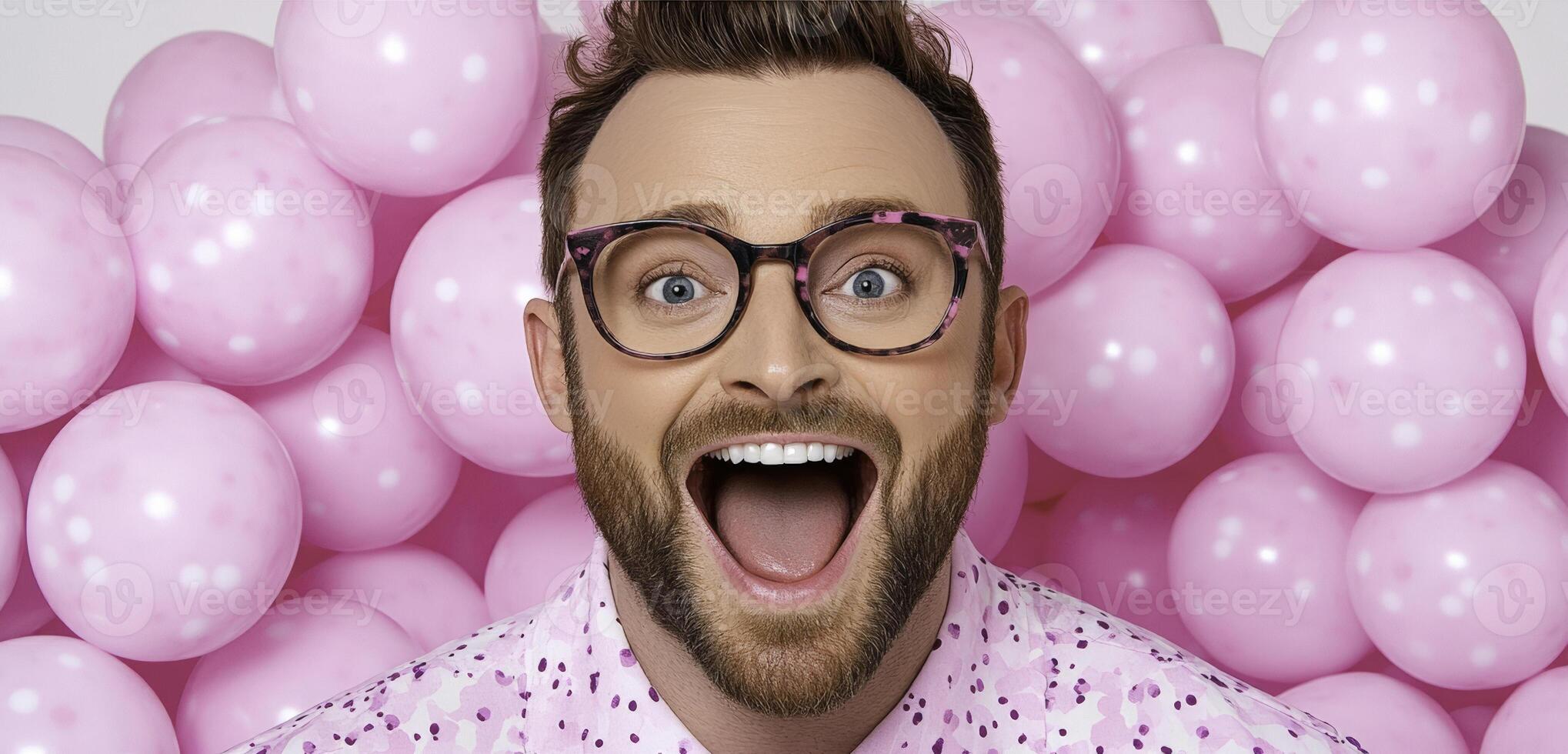 A man with glasses and a pink shirt is smiling in front of pink balloons photo