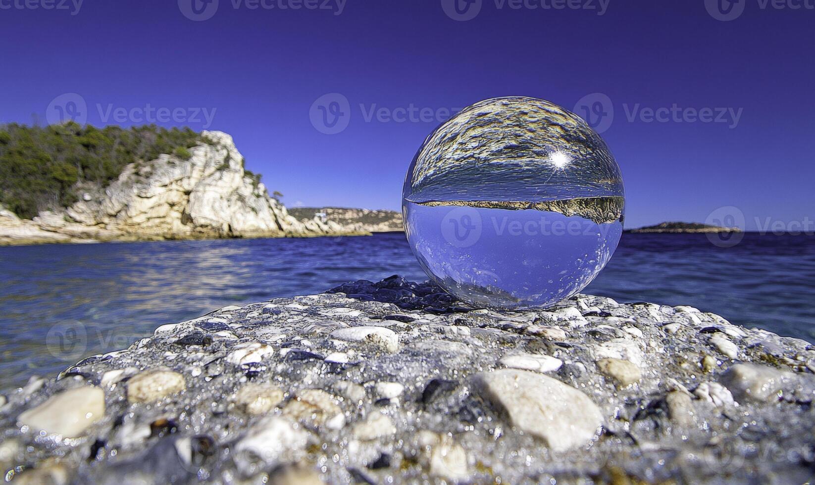 A clear glass ball sitting on a rock near the ocean photo