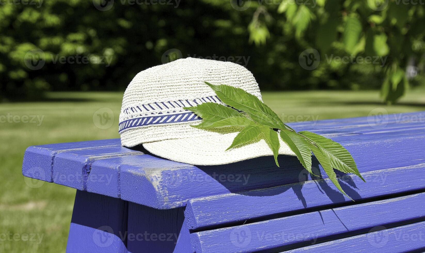 Elegant straw hat resting on a vibrant blue bench in a sunny park, surrounded by fresh green leaves and a serene outdoor atmosphere of nature photo