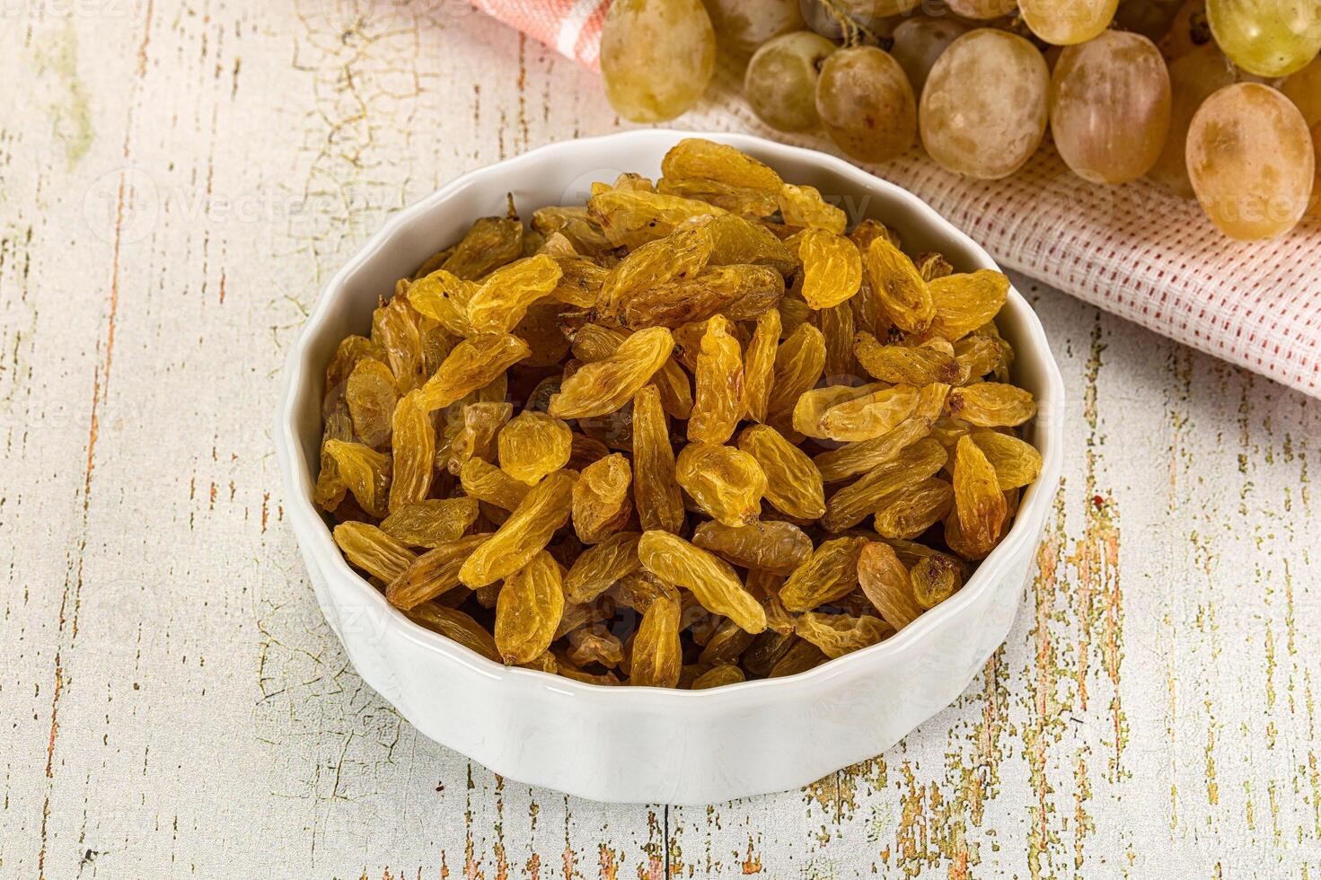 A bowl of raisins sitting on a table next to a bunch of grapes photo