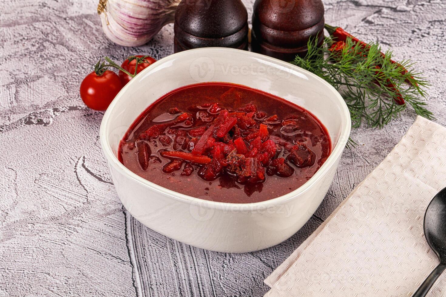 A bowl of red soup with a spoon and some vegetables photo