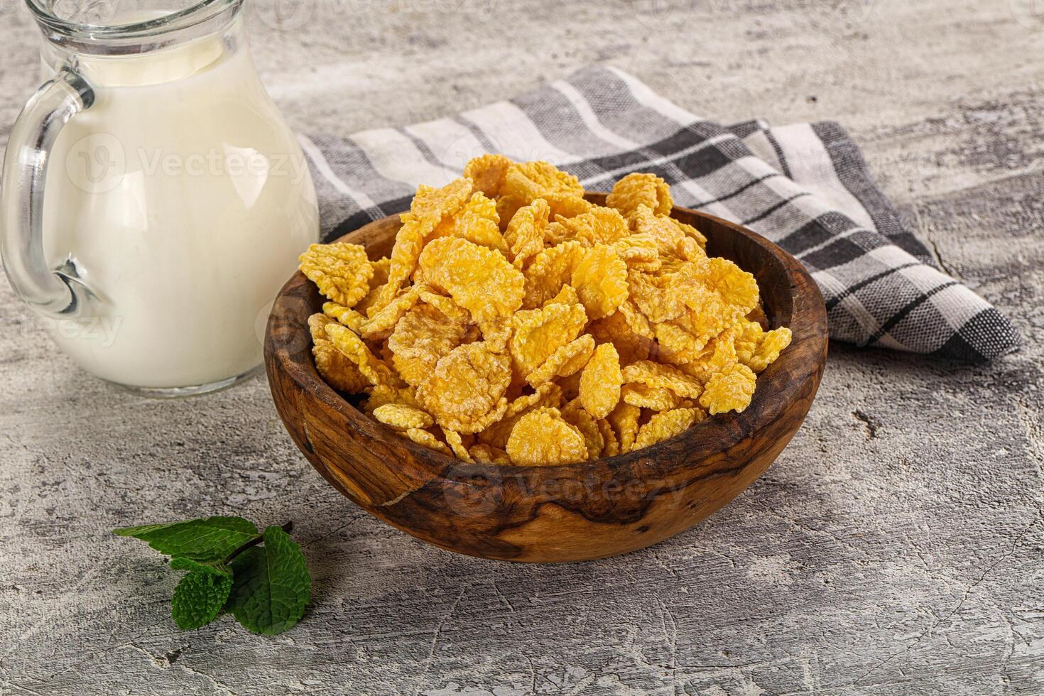 A bowl of cornflakes and a glass of milk on a wooden table photo