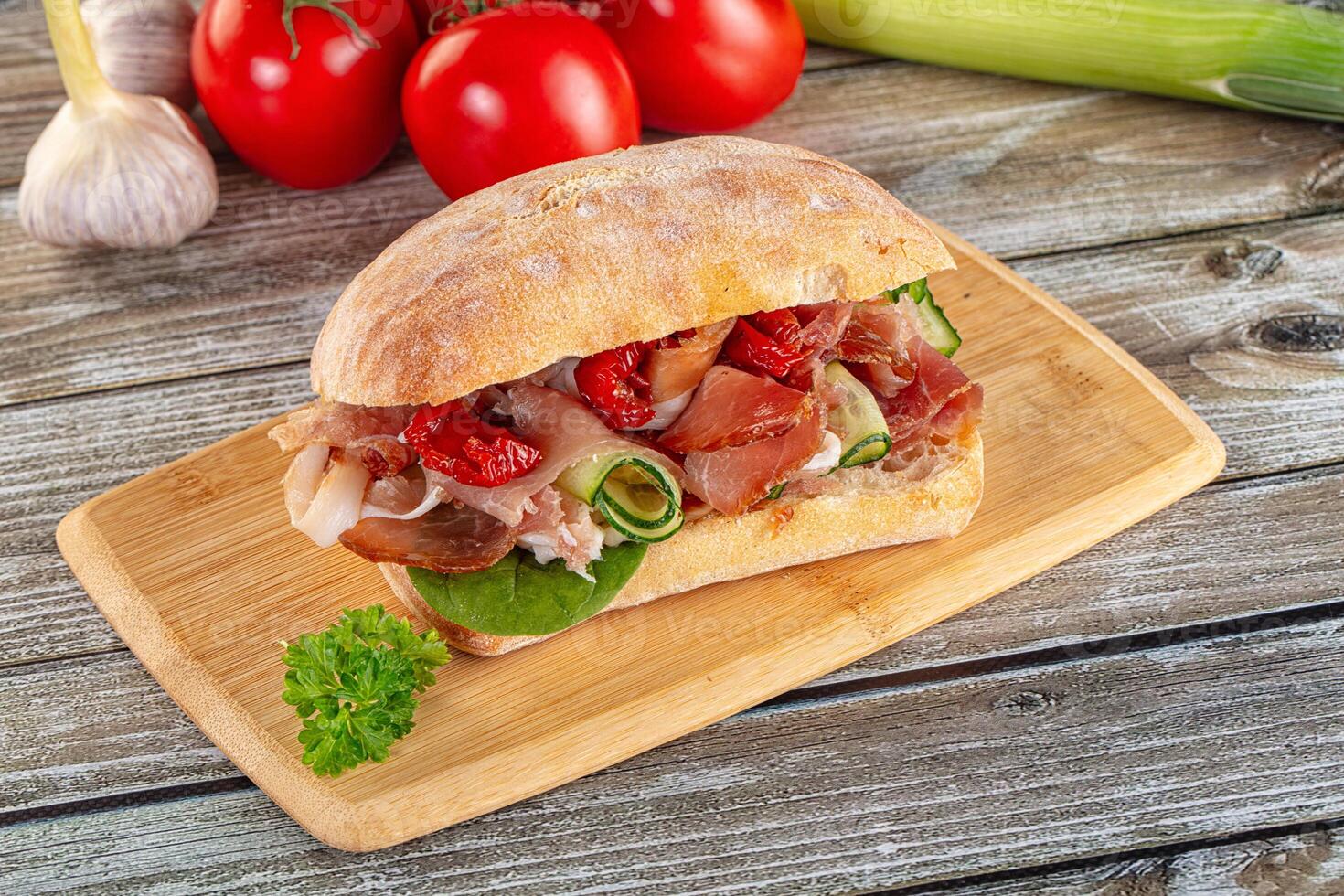 A sandwich with meat, tomatoes and herbs on a wooden cutting board photo