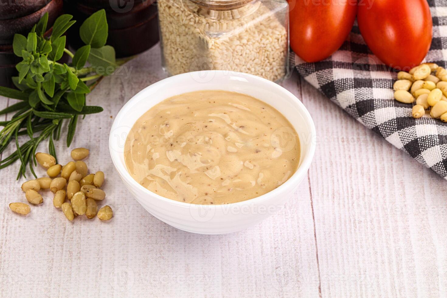 A bowl of dressing sits on a table next to tomatoes, garlic and other ingredients photo