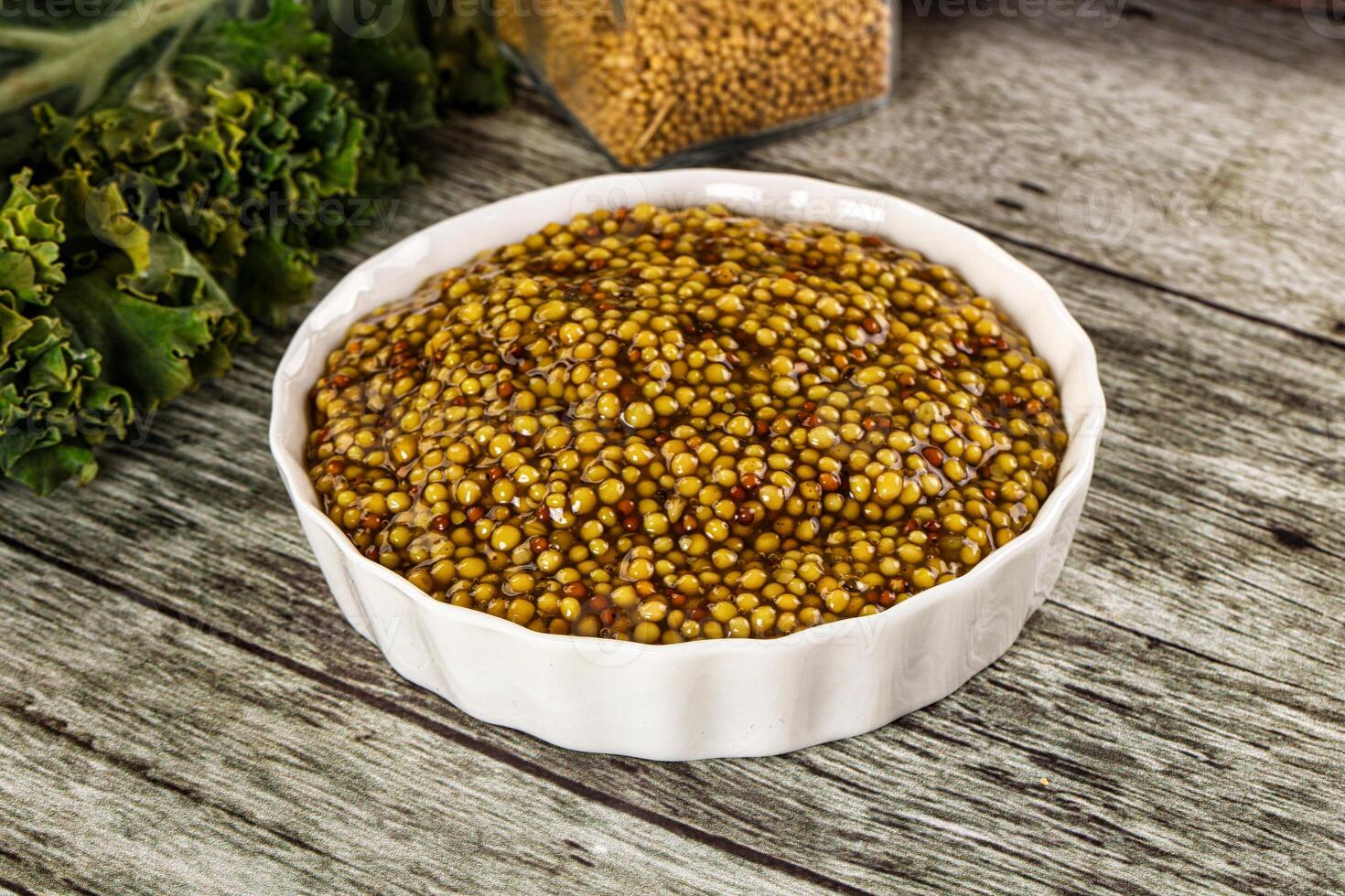 A bowl of mustard on a table next to a bowl of broccoli photo