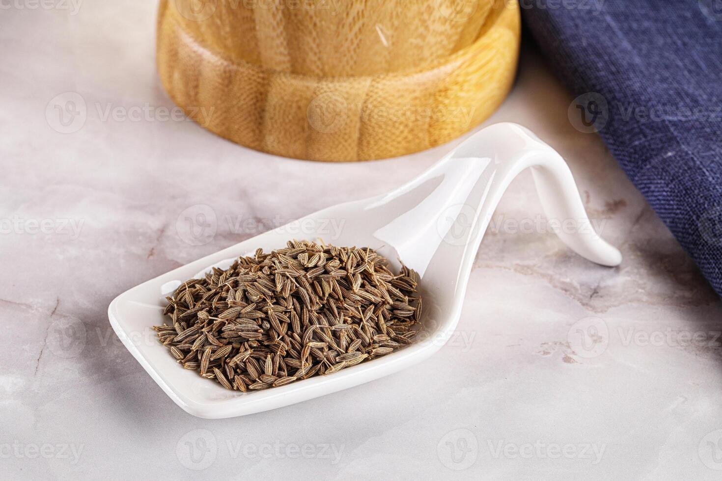 A white ceramic scoop with cumin seeds on a table photo