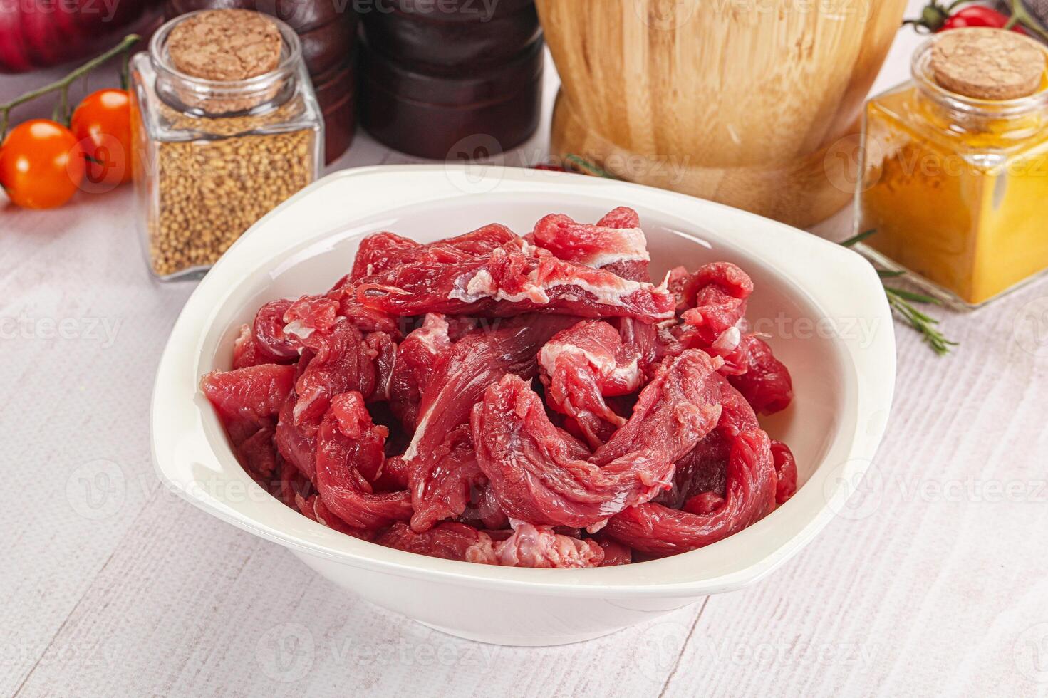 A bowl of raw meat sitting on a table next to a bottle of spices photo