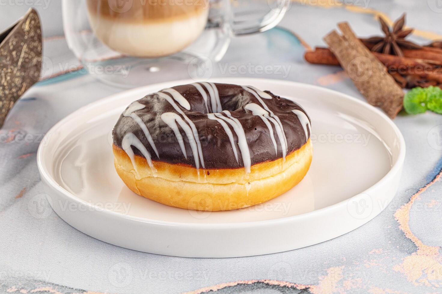 A chocolate glazed donut on a plate next to a cup of coffee photo