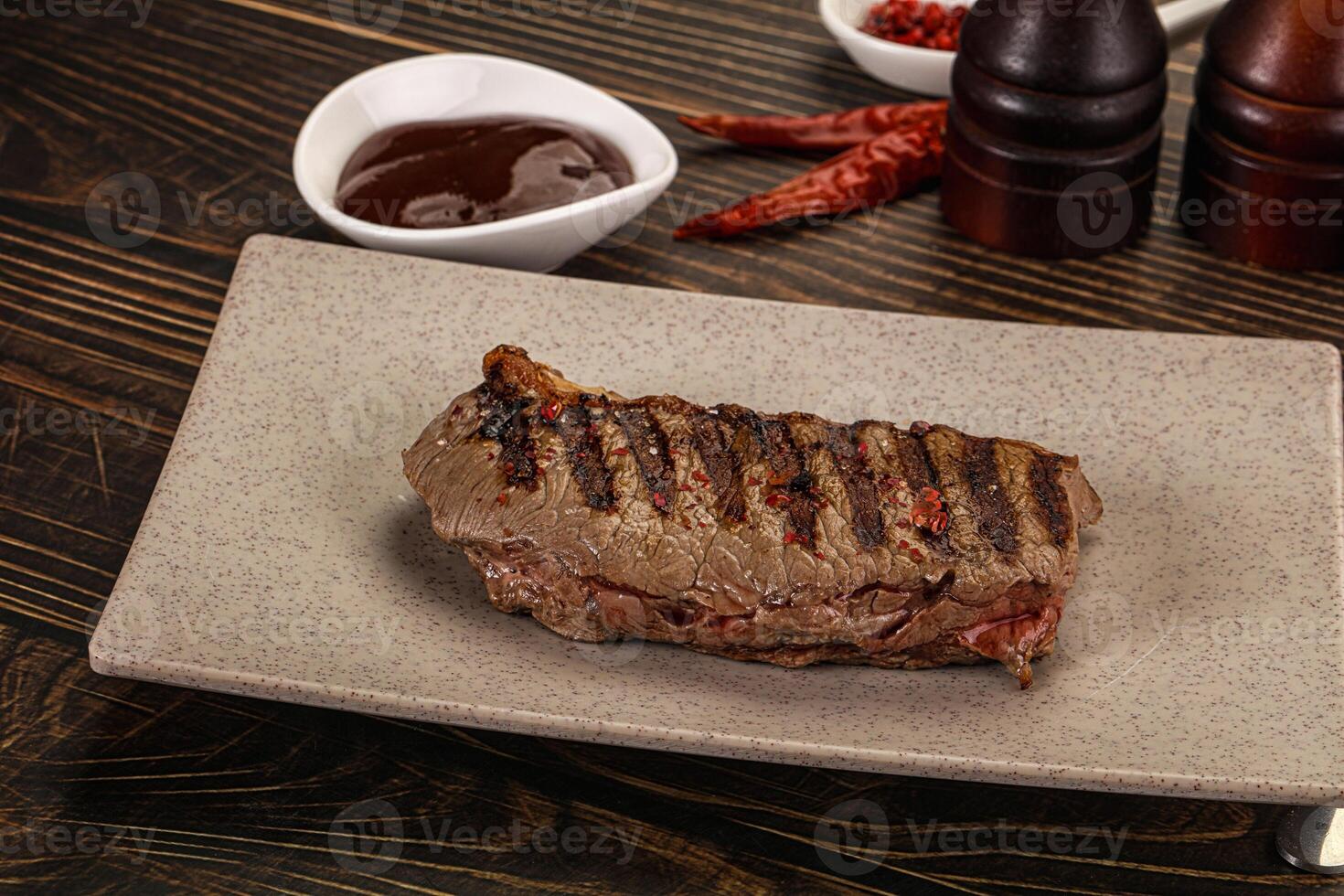 A steak on a plate with a bottle of ketchup and a bottle of hot sauce photo