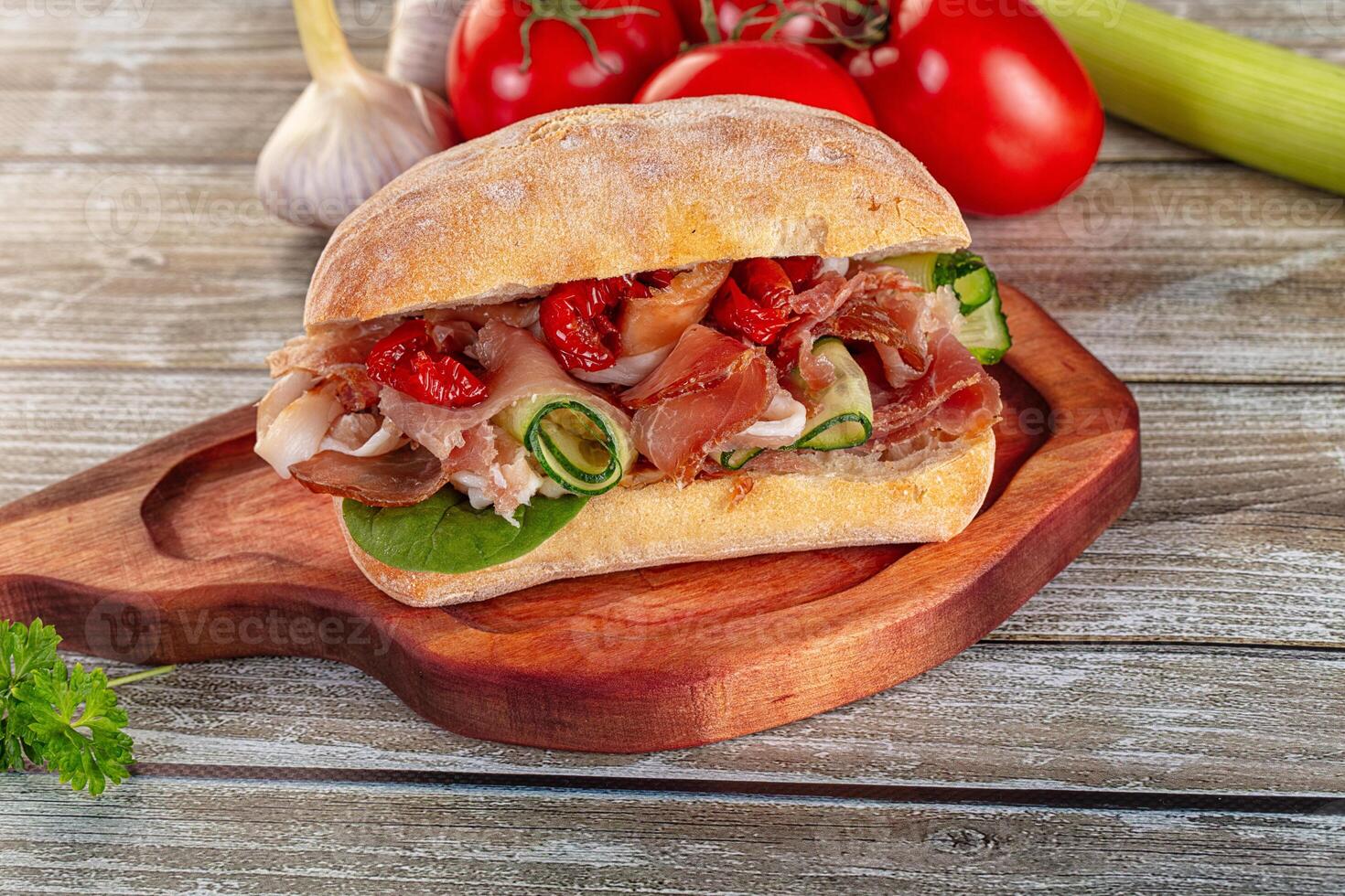 A sandwich on a wooden cutting board with vegetables and tomatoes photo