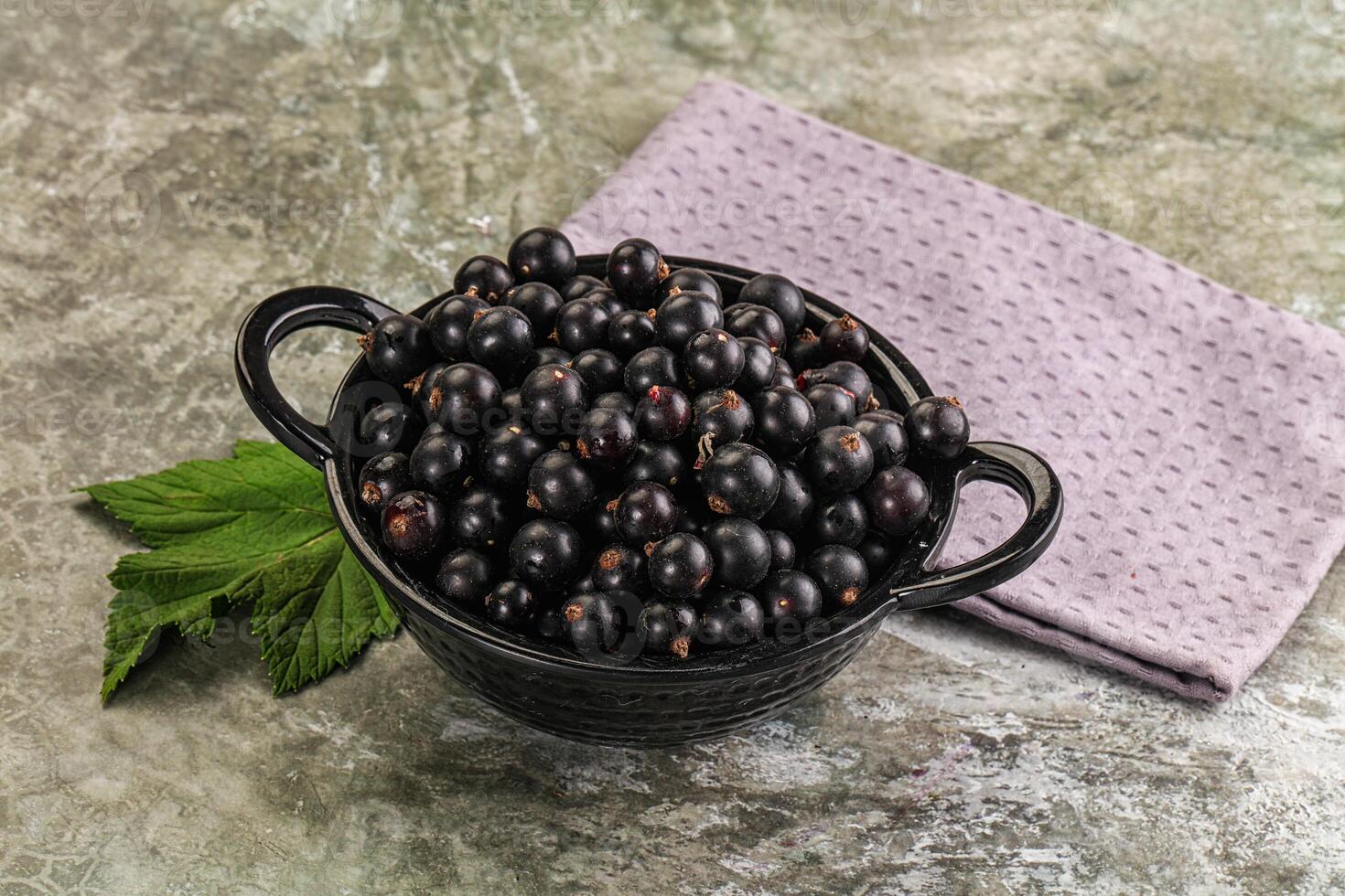 Black currant in a black bowl with a purple napkin on a gray background photo