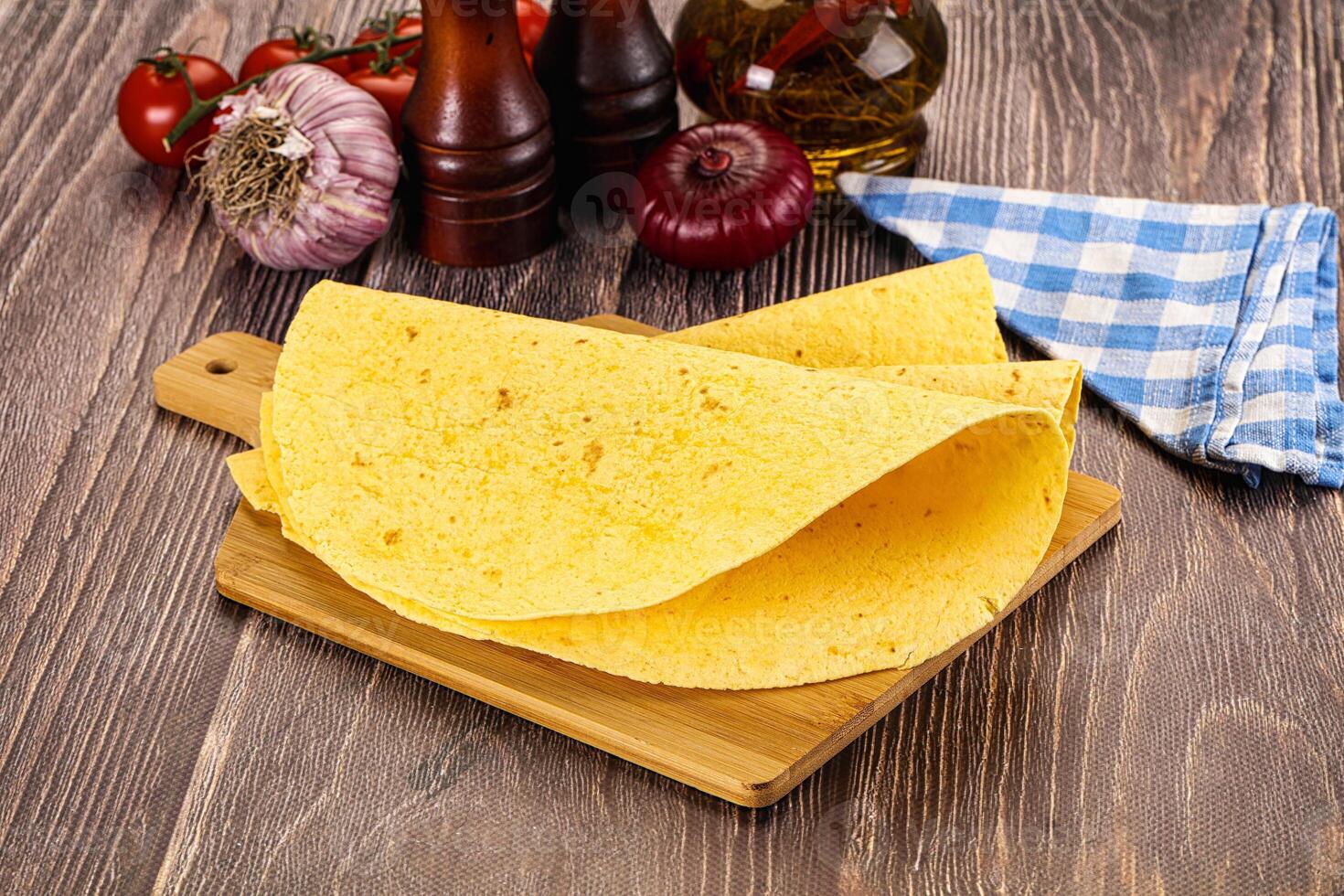 A tortilla on a cutting board with tomatoes, onions and garlic photo