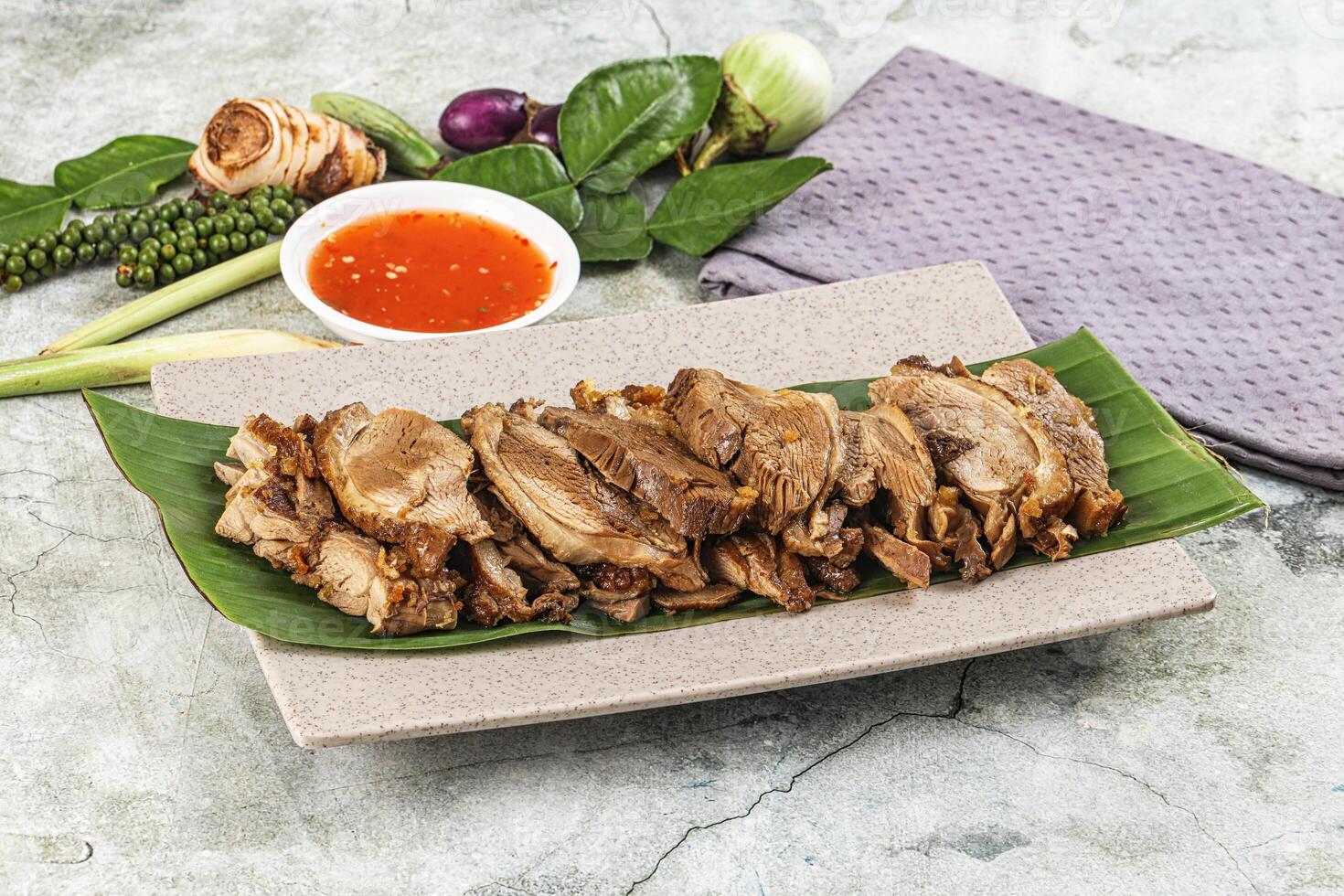 A plate of meat on a leaf with sauce and vegetables photo