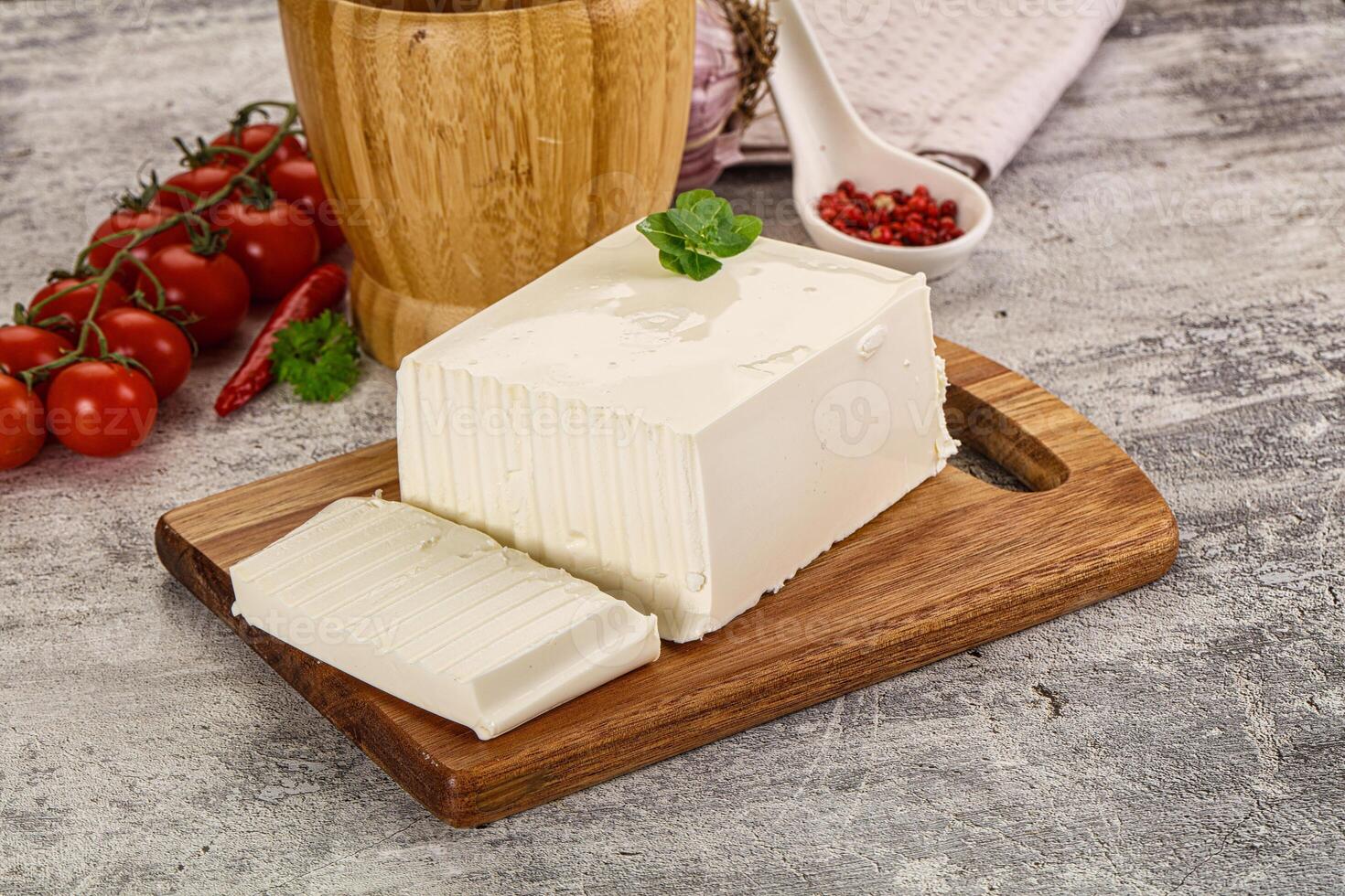 A piece of cheese on a cutting board next to a jar of tomatoes photo