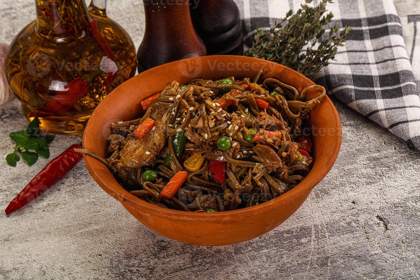 A bowl of noodles with vegetables and a bottle of olive oil photo