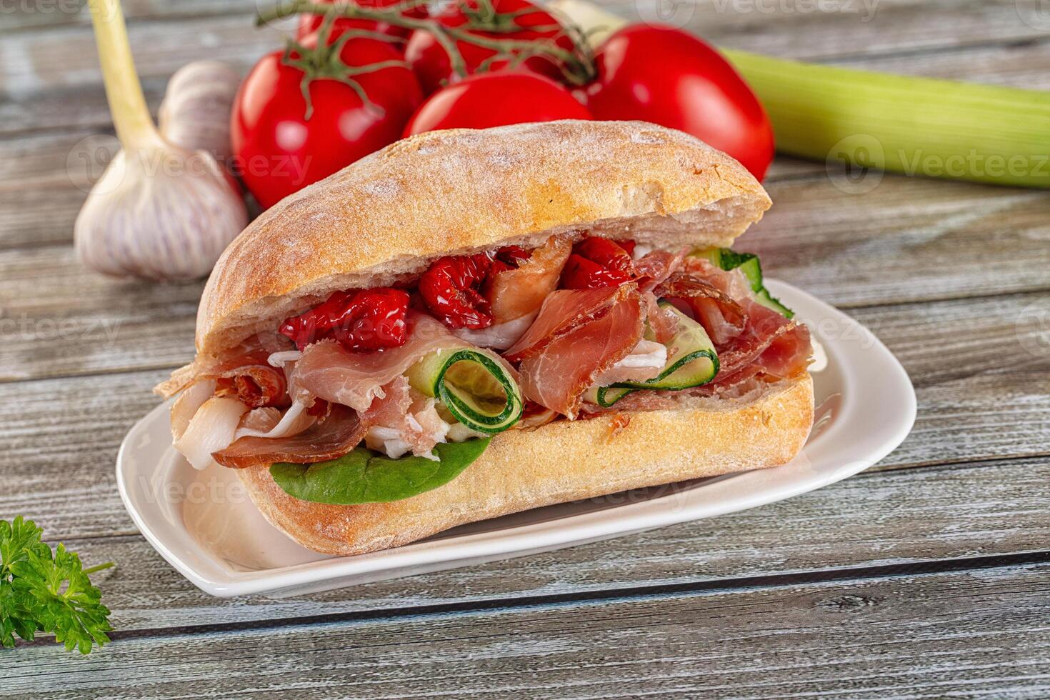 A sandwich with meat, vegetables and tomatoes on a plate photo