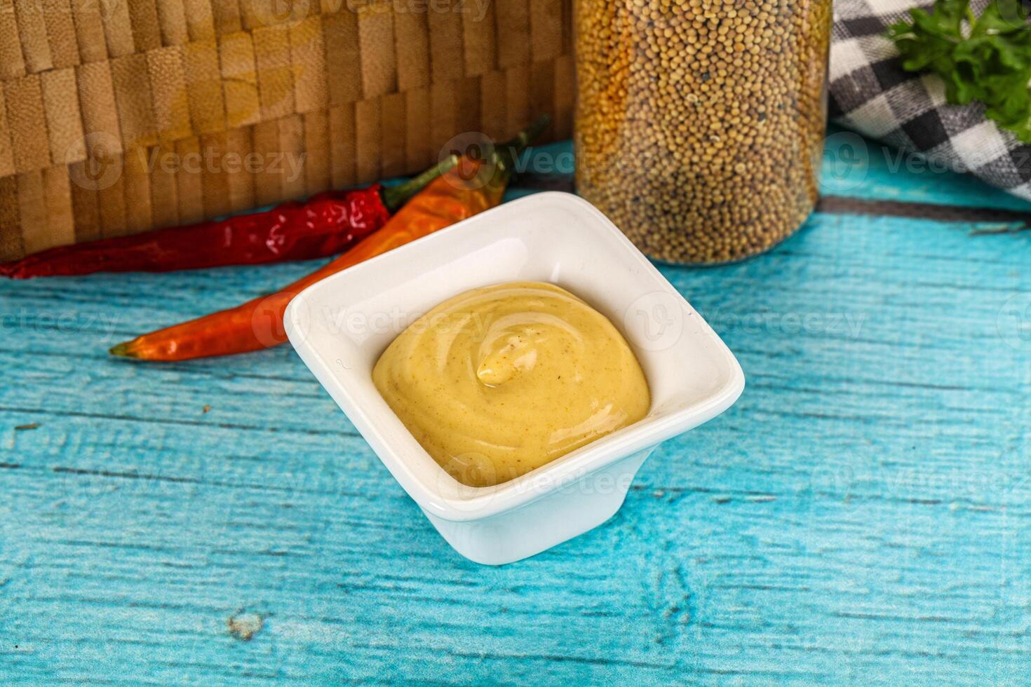 A bowl of mustard sauce with chili peppers and herbs on a blue table photo