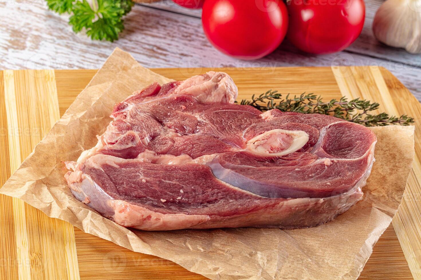 A piece of meat on a cutting board with herbs and vegetables photo