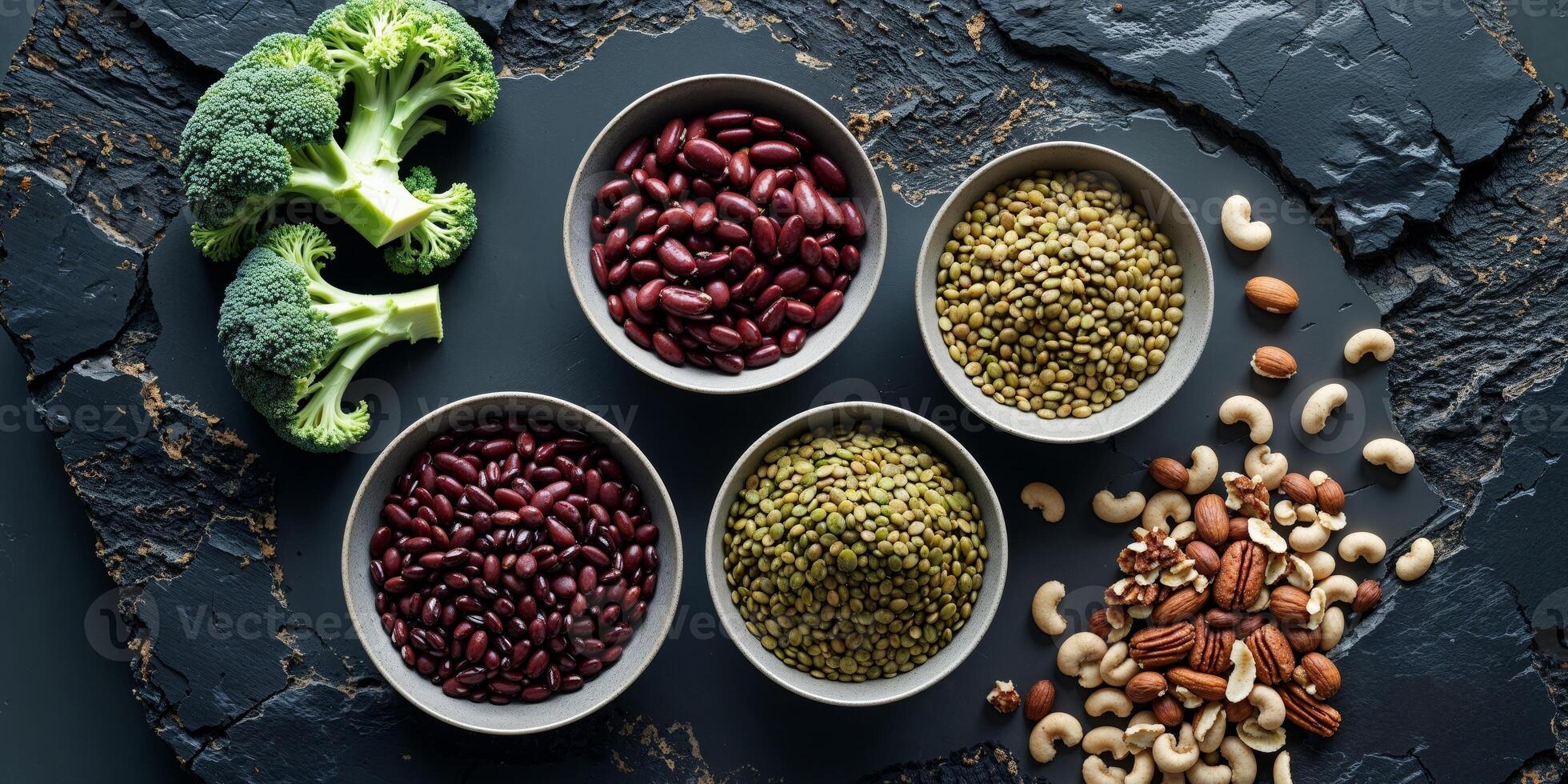 Overhead view of bowls filled with broccoli beans lentils and nuts on a dark textured surface photo