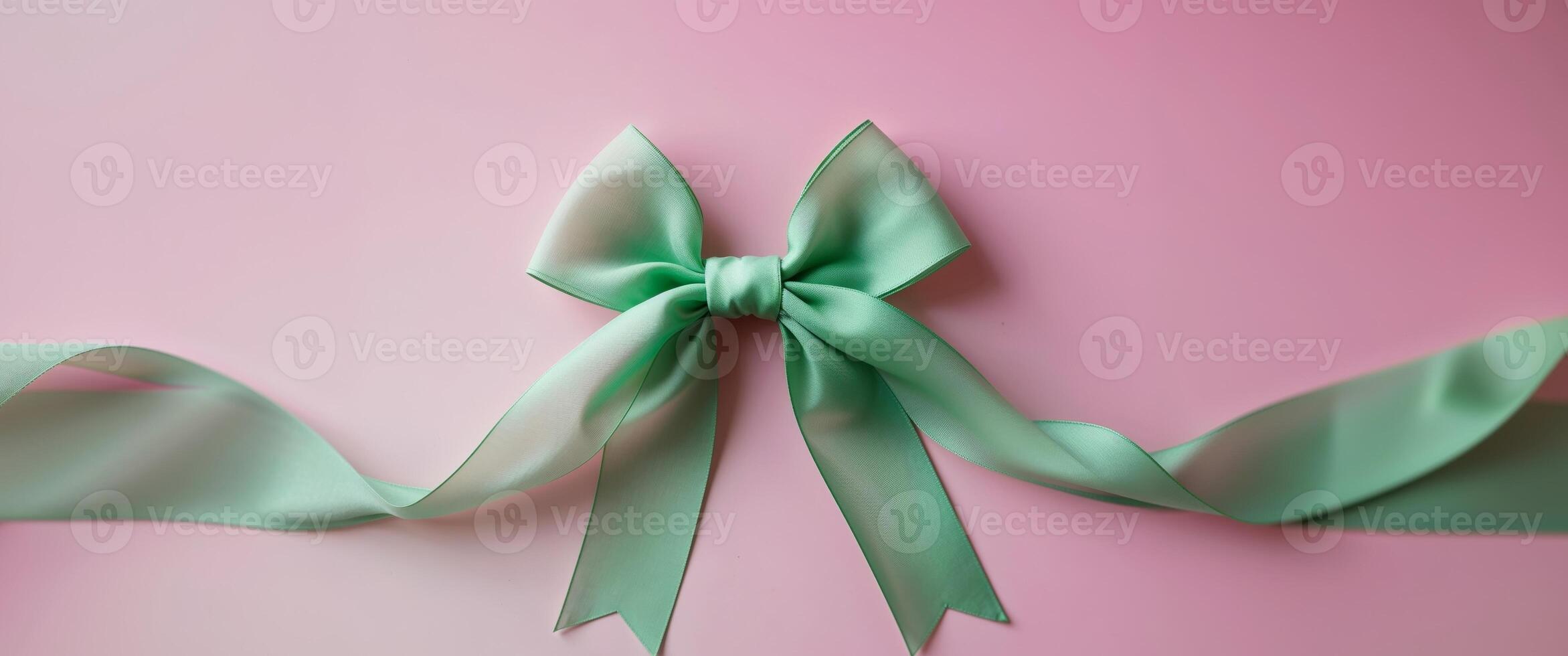 green ribbon tied in a bow on a pink background. photo