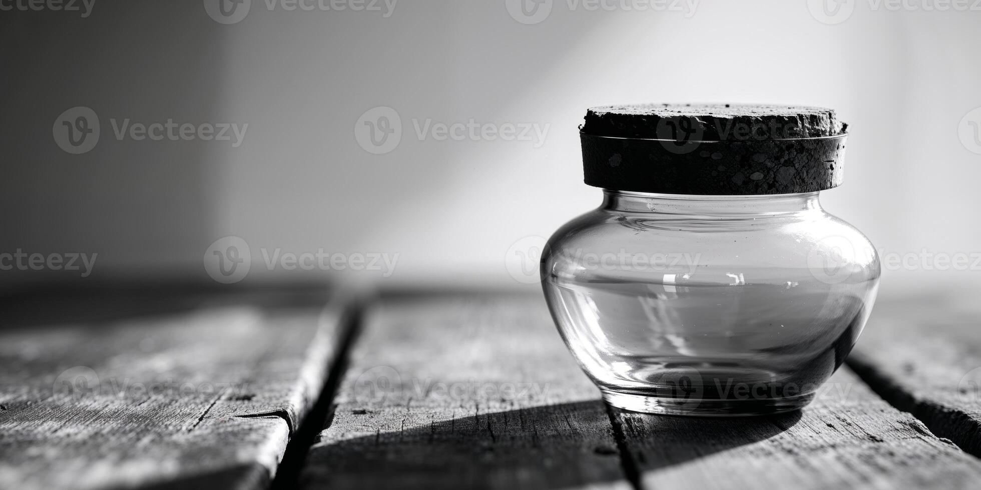 A black and white photo of a glass bottle on a wooden table