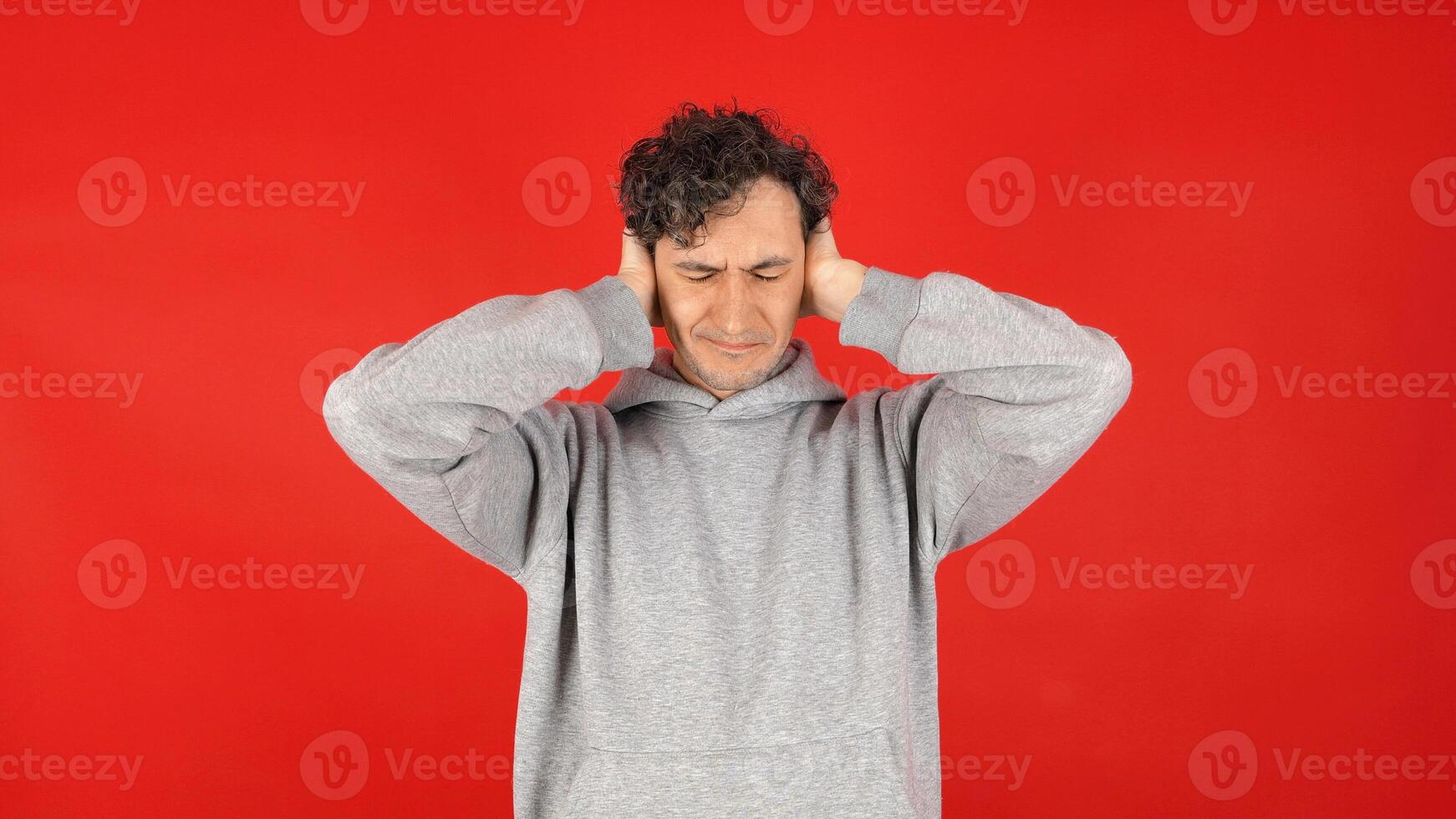 unhappy, angry, suffering man covers ears with palms, does not want to listen to screams, loud music, avoids stress. Isolated on red background of studio shot photo