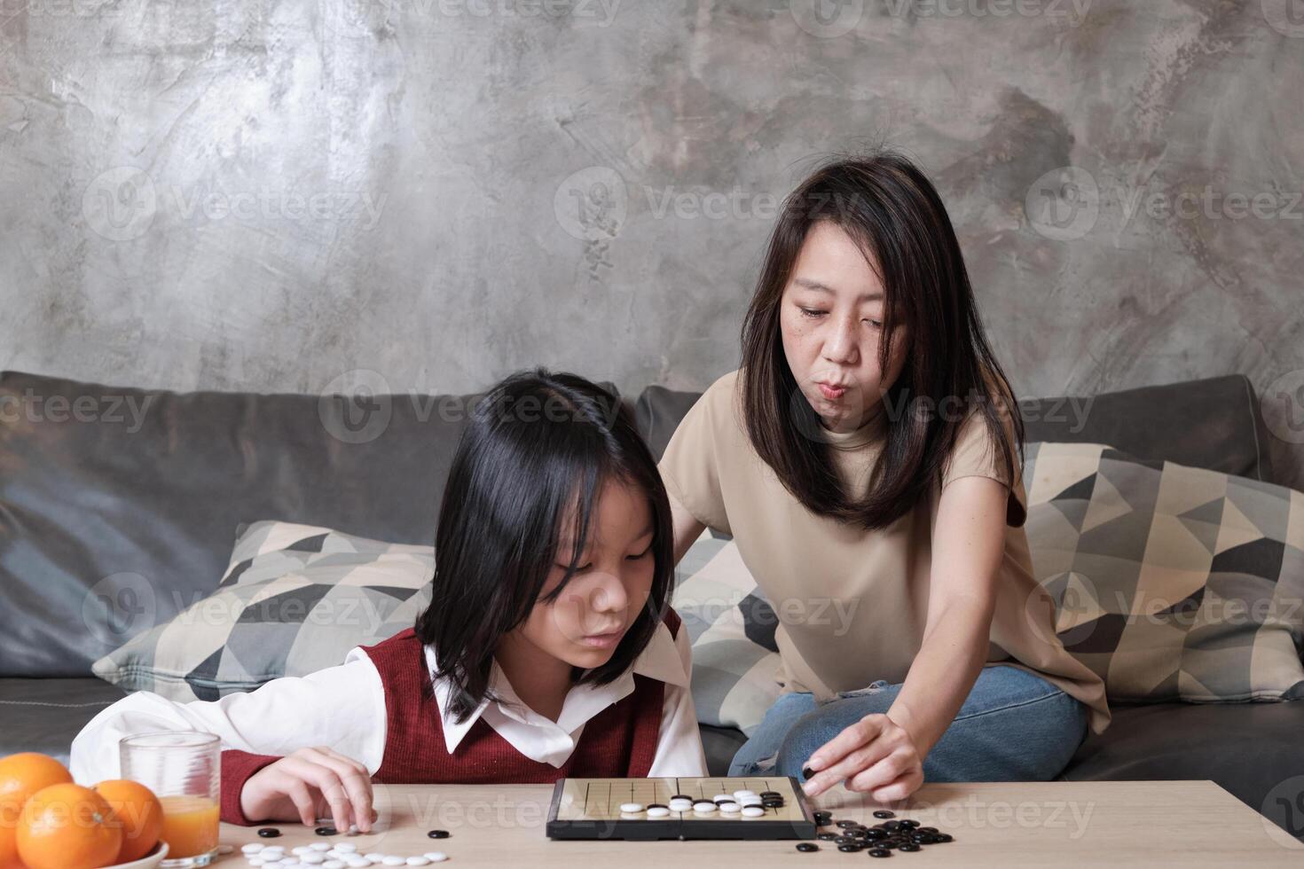 Asian family times, mother, and girl fun playing Go, checkers board game on table in home living room together with love and cheerful, happy weekend relaxing hobby of child and parent. photo