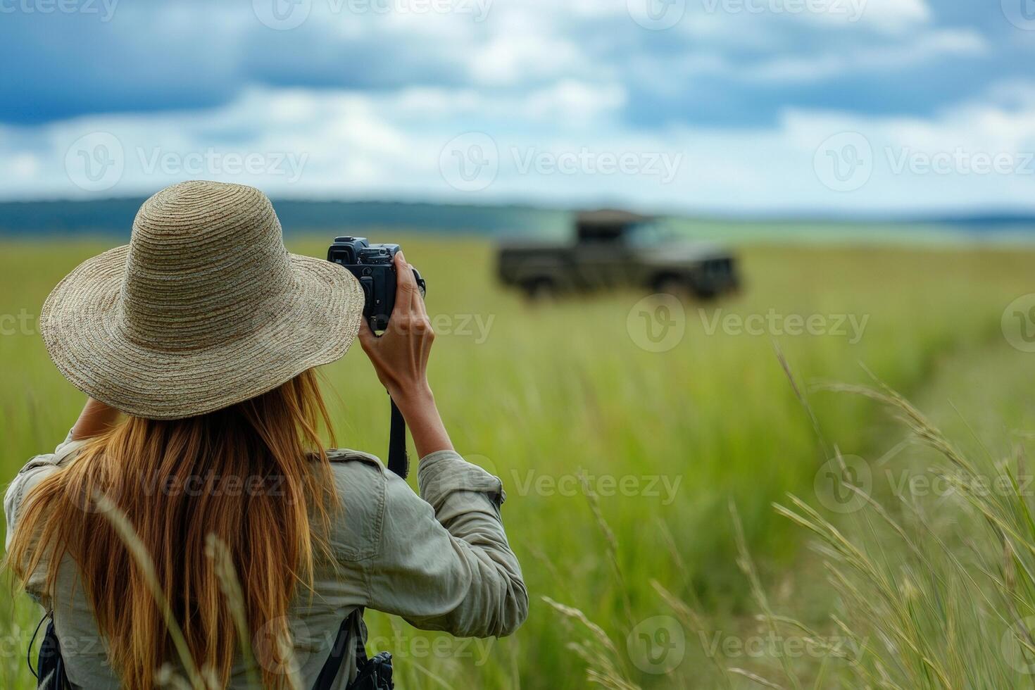 Female photographer capturing wildlife in vast grassland with cloudy skies photo