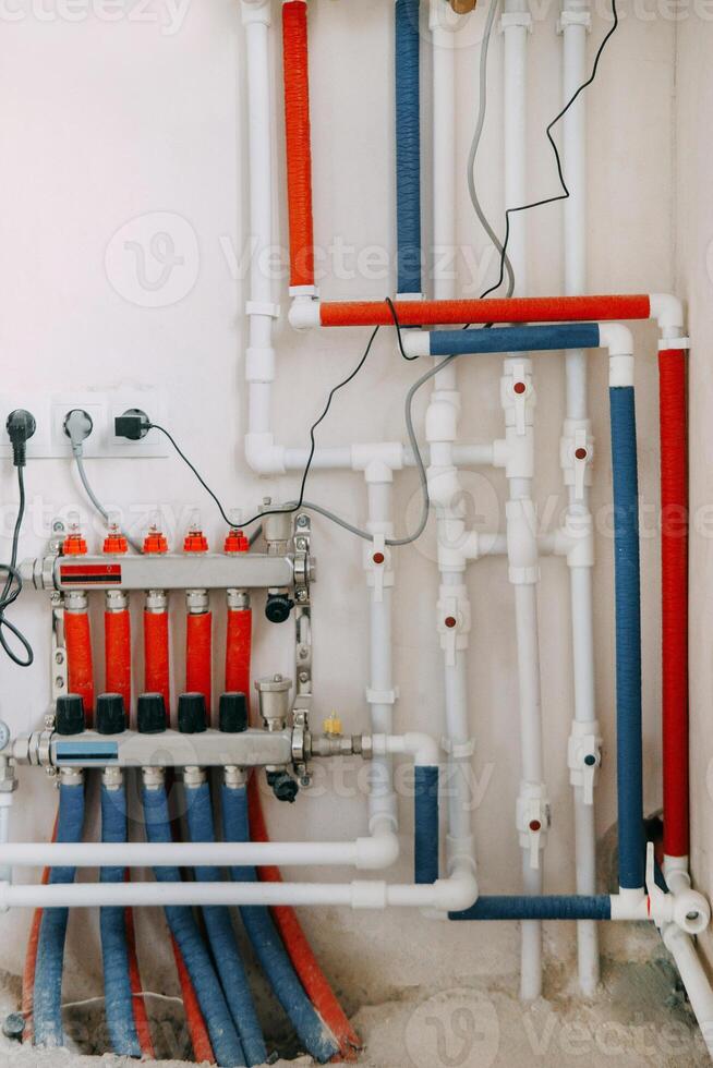 Detailed view of an intricate heating system setup featuring red and blue color-coded pipes, valves, and gauges. Connection diagram of gas boiler with underfloor heating photo