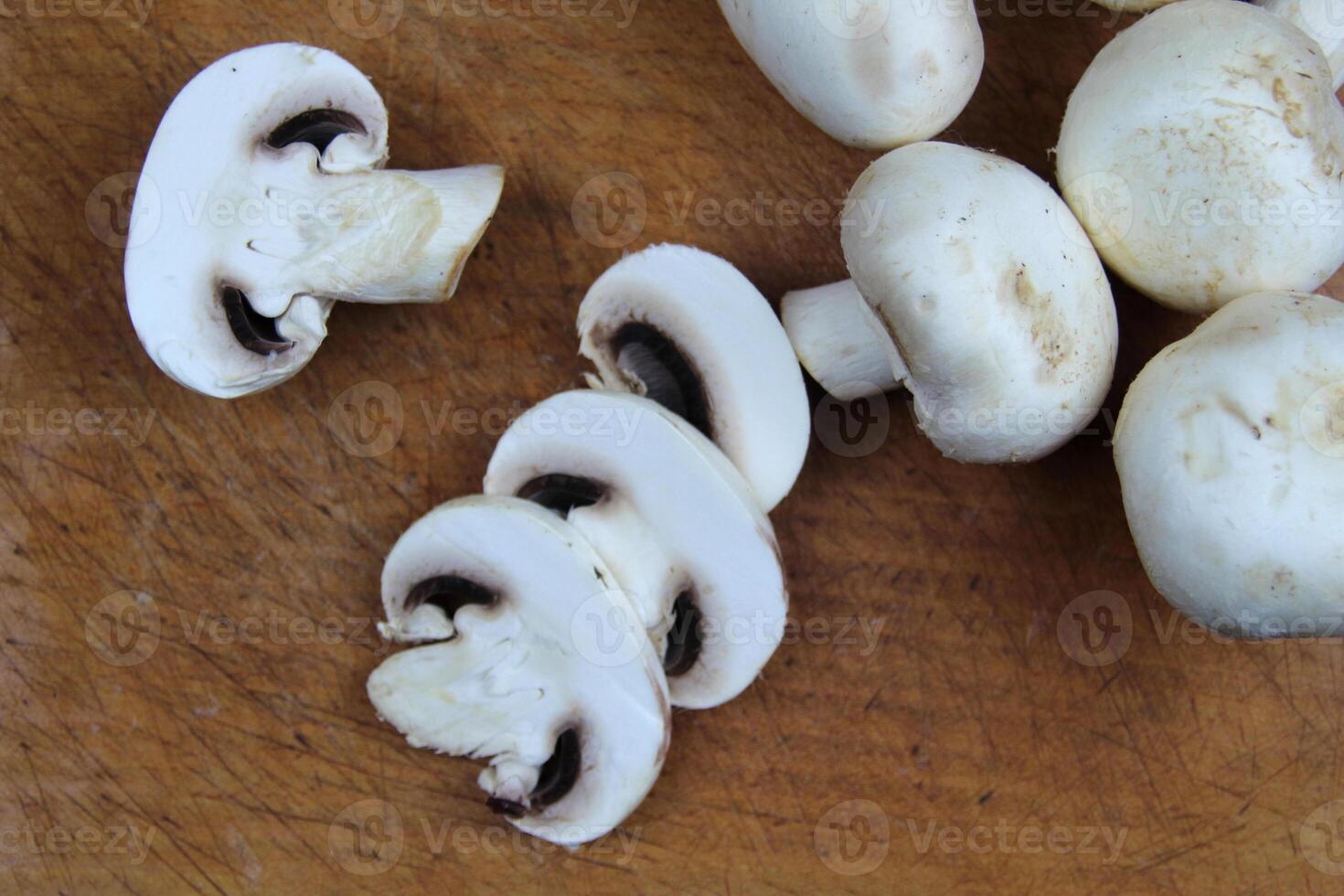 Sliced mushrooms lie on a wooden board, in the background are whole large champignons photo