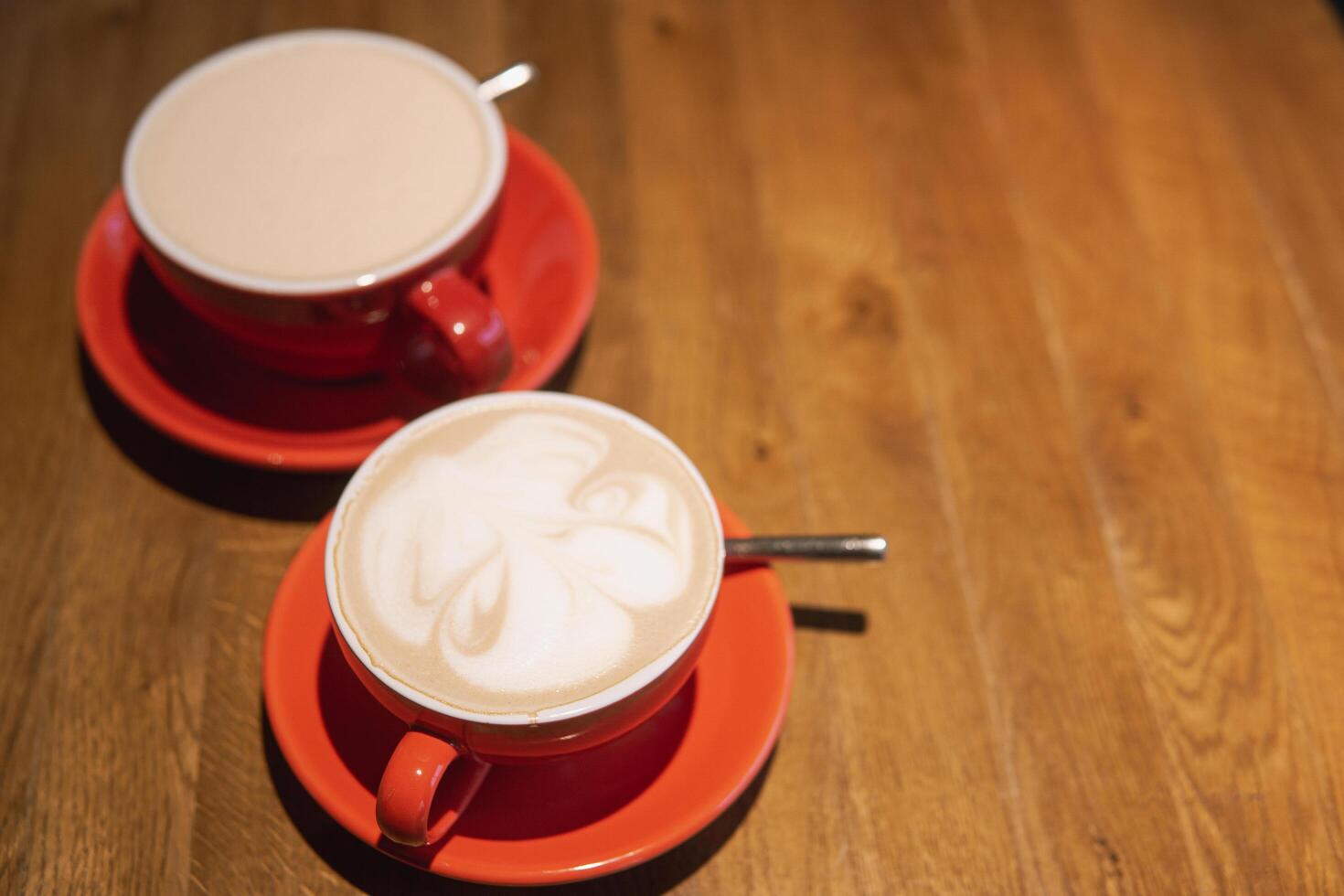 Artistic latte creations served in red cups on wooden table. A perfect representation of a cozy cafe atmosphere for coffee lovers photo