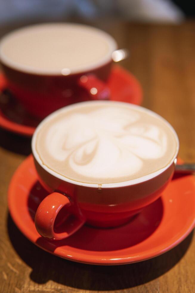 Cups of coffee in vibrant red ceramic mugs with intricate surface designs, resting on a smooth wooden table, evoking warmth and inviting sharing moments photo