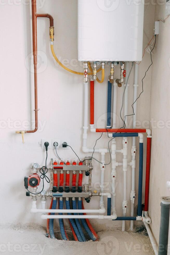 Detailed view of an intricate heating system setup featuring red and blue color-coded pipes, valves, and gauges. Connection diagram of a gas boiler with a underfloor heating system photo