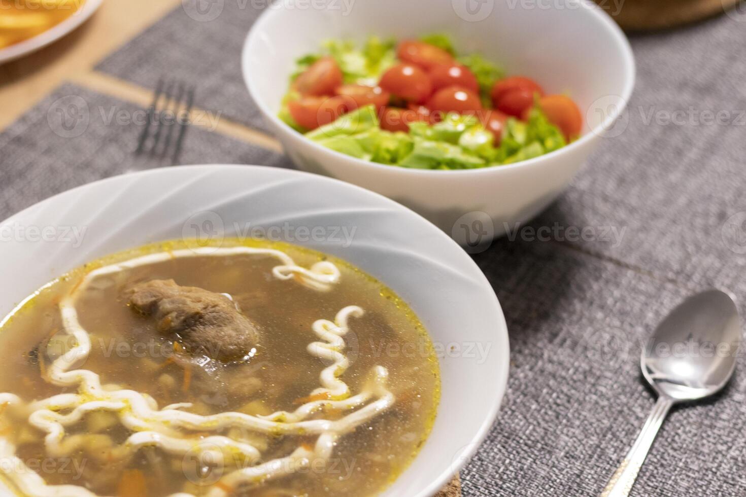 Bawl with cherry tomatoes and lettuce leaves, bawl with soup next to it photo